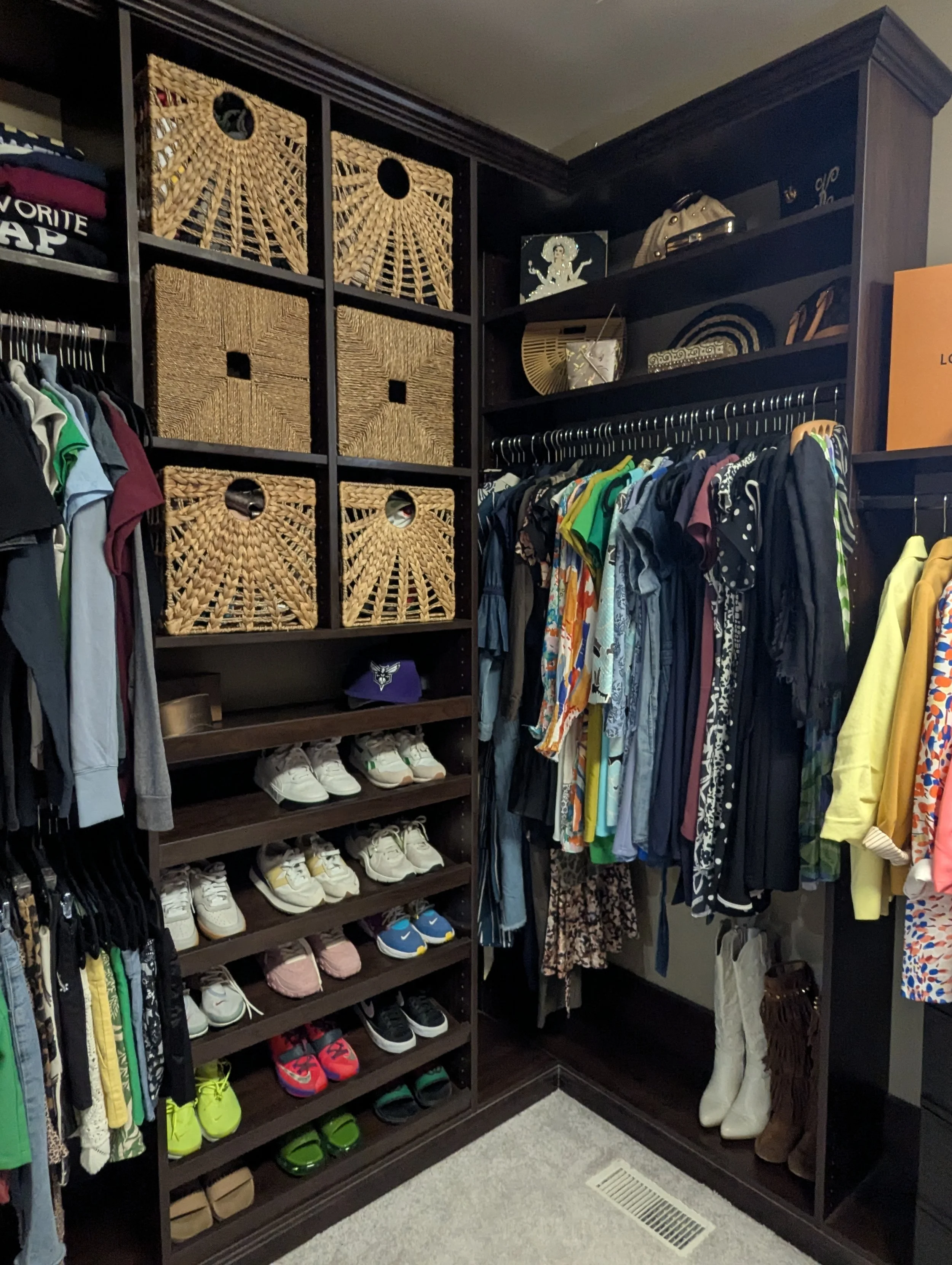 Walk-in closet with hanging clothes, shelves of shoes, and woven storage bins.