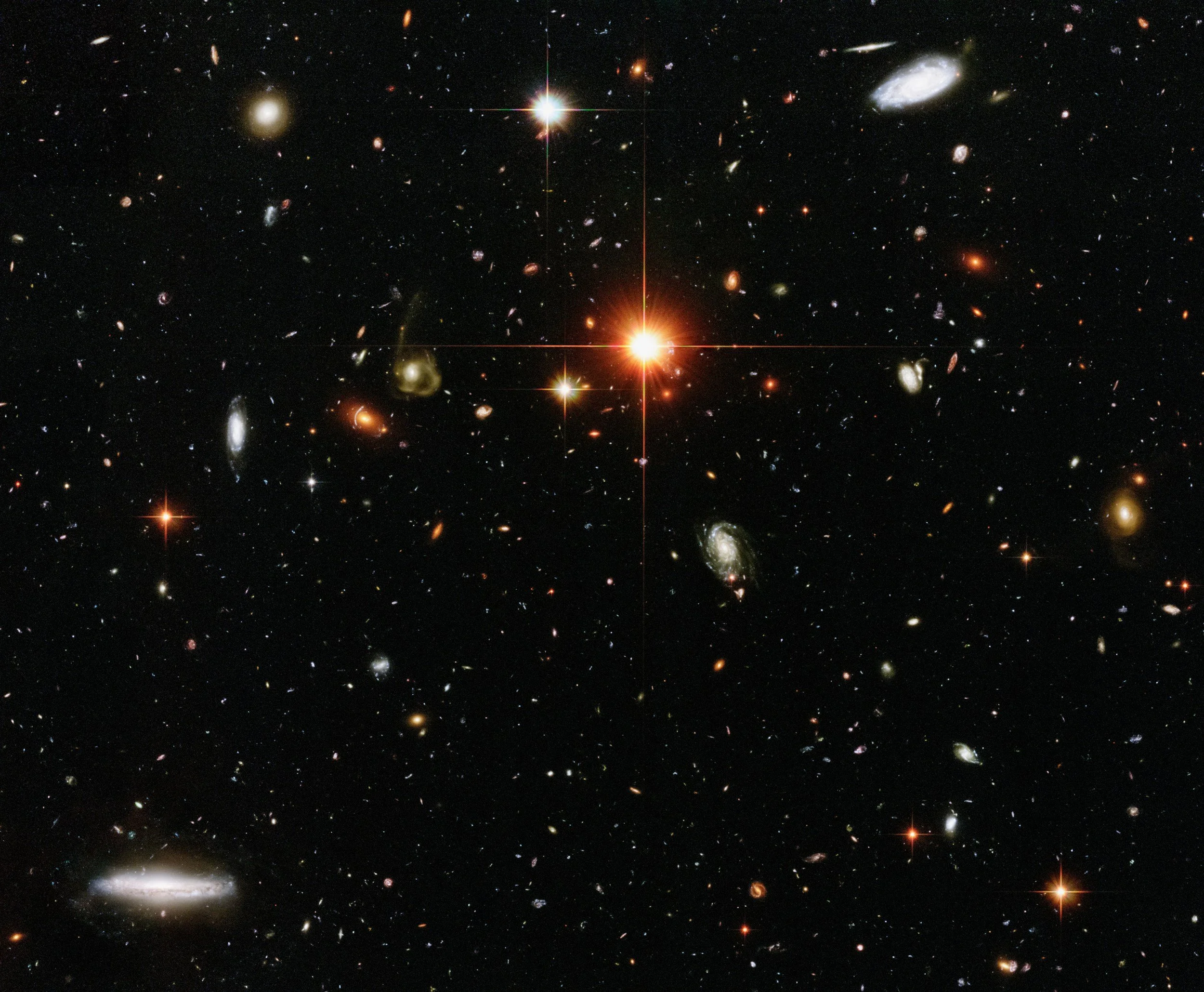 Bild av många avlägsna galaxer och stjärnor i rymden med en centralt belägen stark ljuskälla.