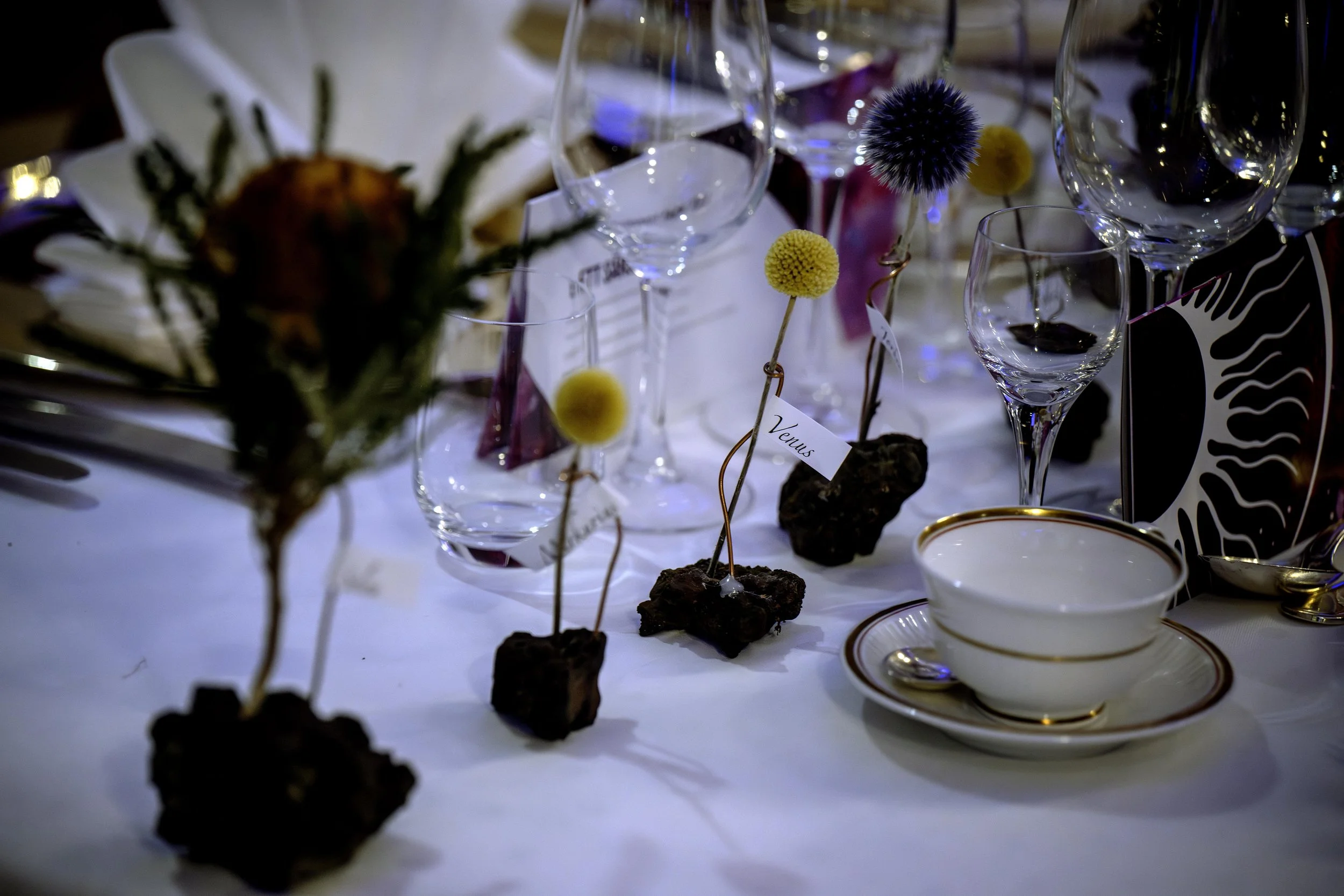Ett bord dukat med tomglas, vinglas, en kopp och små dekorationer med blommor och stenar.
