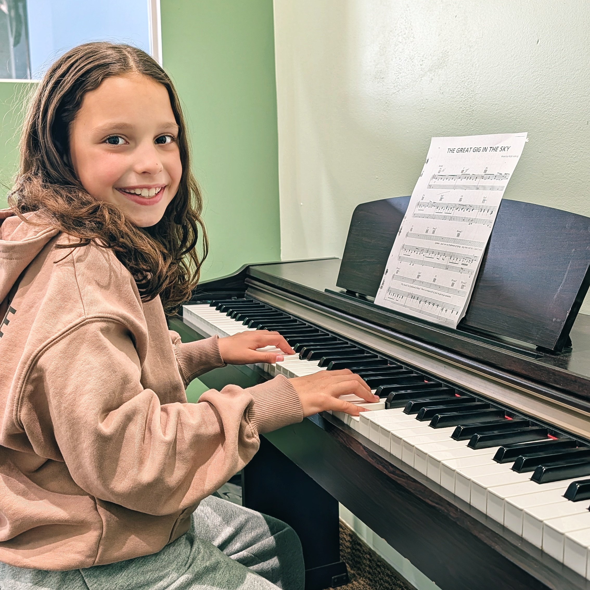 A young student smiling while playing the piano at Noteworthy Music Academy in West Bloomfield.