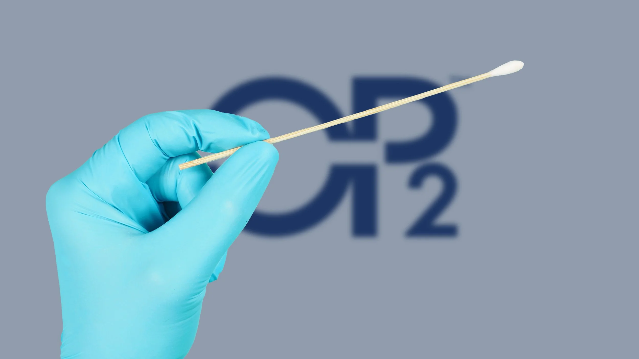 A hand in a blue medical glove holding a cotton swab or Q-tip in front of a blurred background with a symbol for carbon dioxide, CO2, in dark blue.