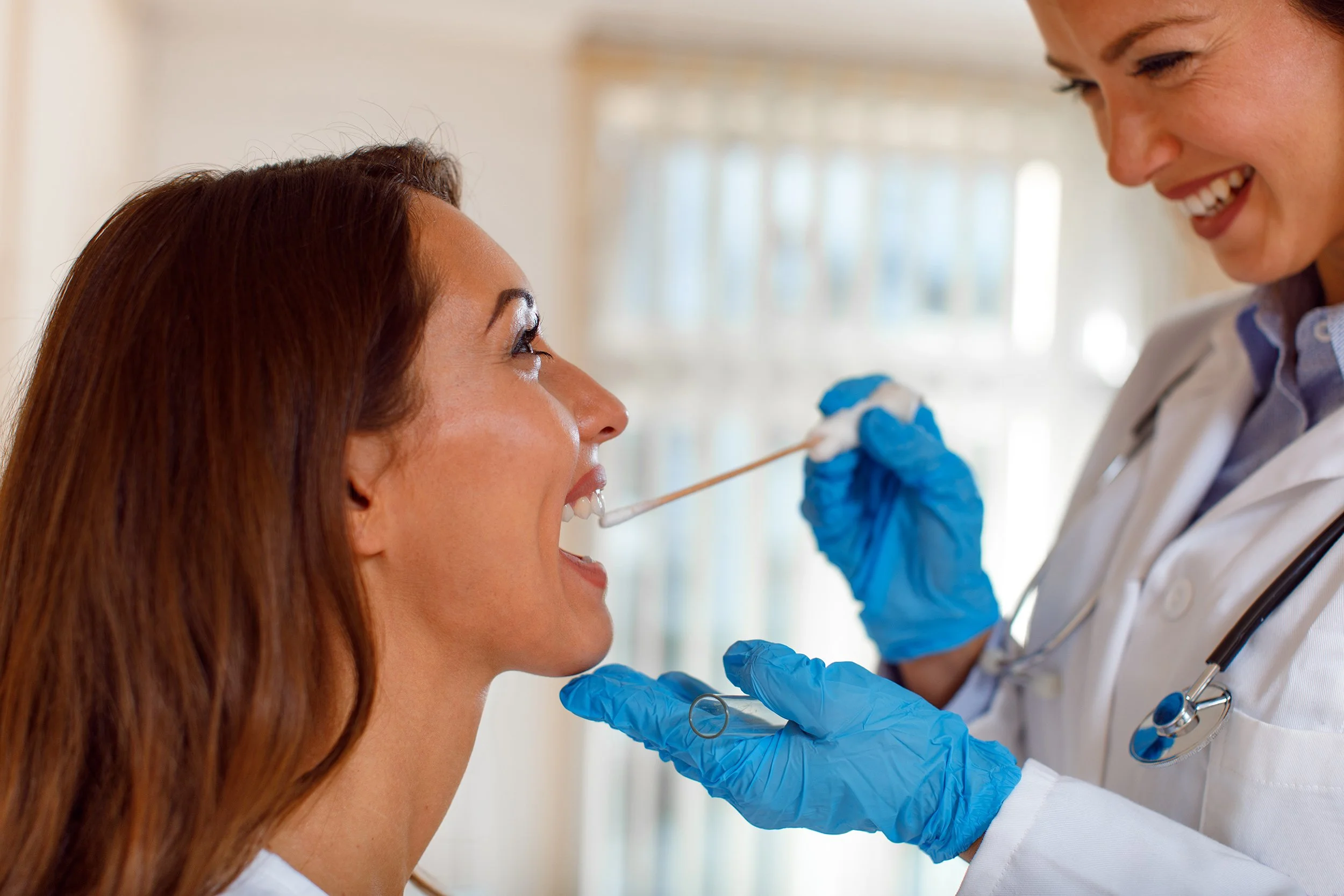 A healthcare professional in blue gloves administering a throat swab test to a woman with long red hair inside a medical clinic.