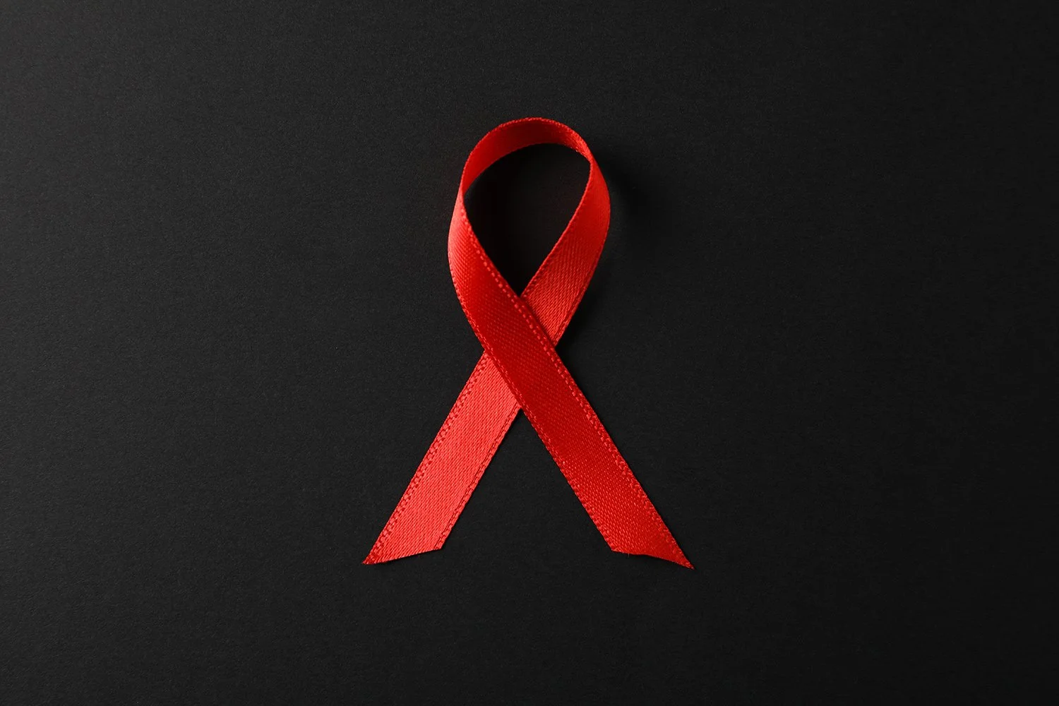 A red ribbon looped in the shape of an awareness symbol on a black background.