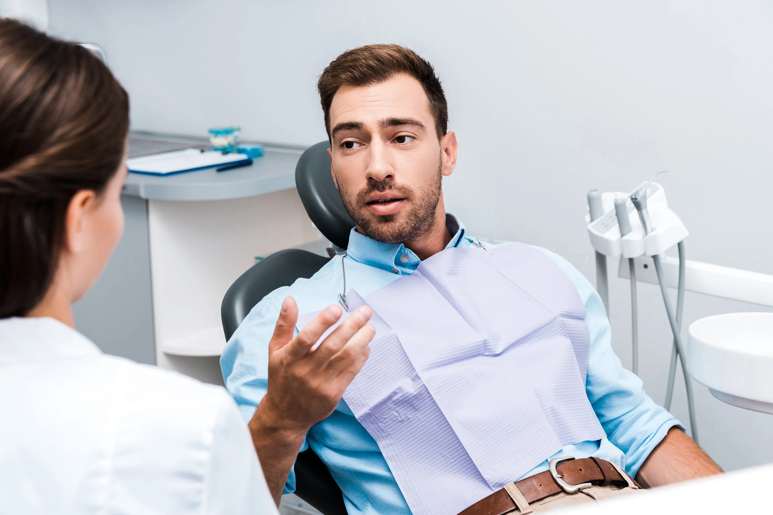 A young man in a dental chair engaging in conversation with a female dentist in a dentist's office.