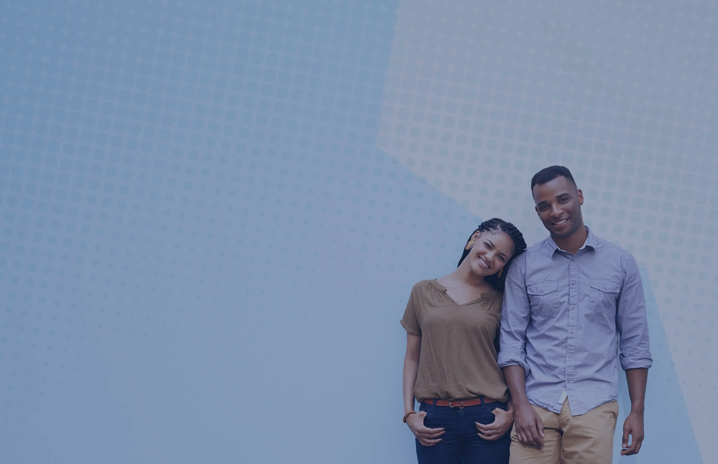 A smiling woman with braided hair and a man with short hair standing close, holding hands, against a blue background with a dotted geometric pattern.