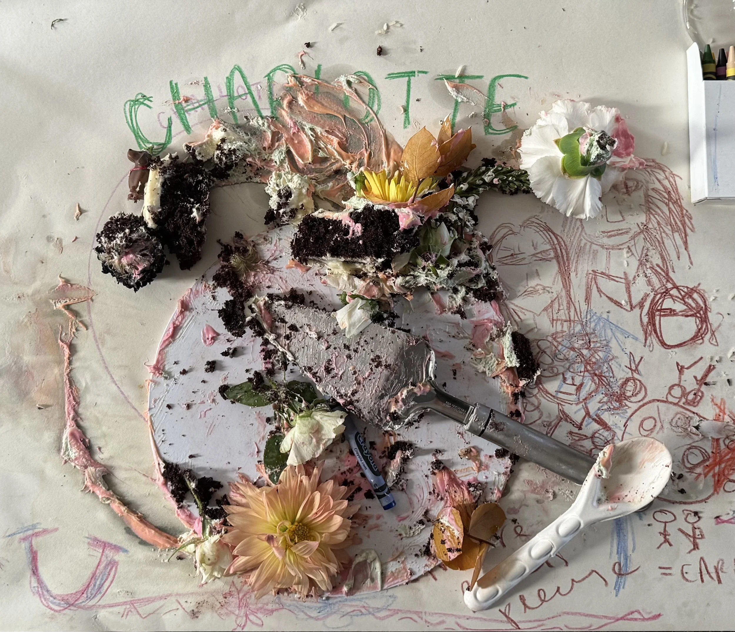 Messy table with cake remnants, flowers, scraped frosting, and children's drawings.