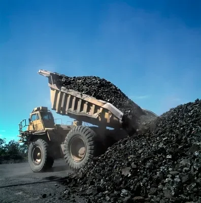 A dump truck unloading a pile of black gravel or coal in an open area with a clear blue sky.