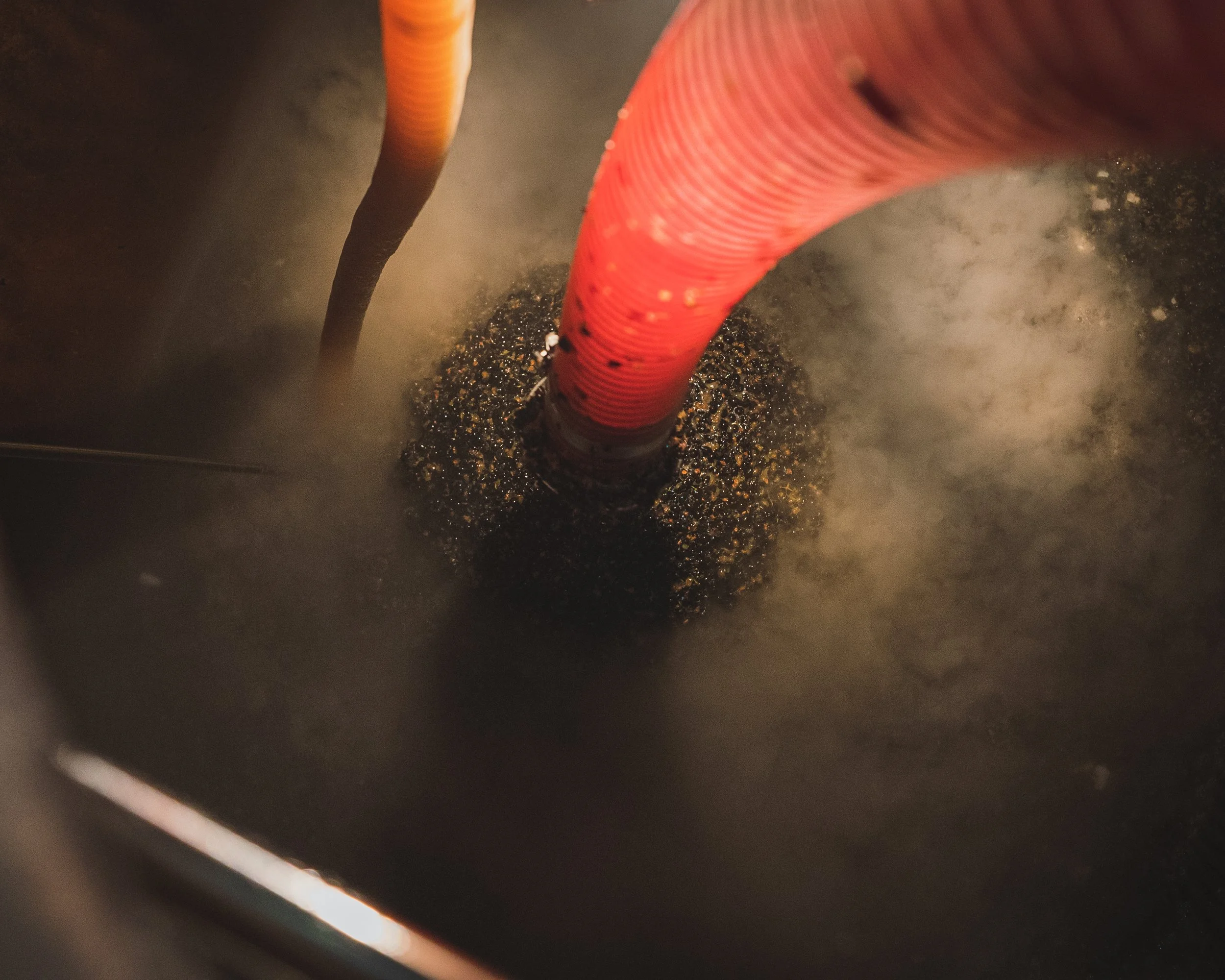 Close-up of two electrical wires, one orange and one black, emitting steam or smoke underneath a dark surface.