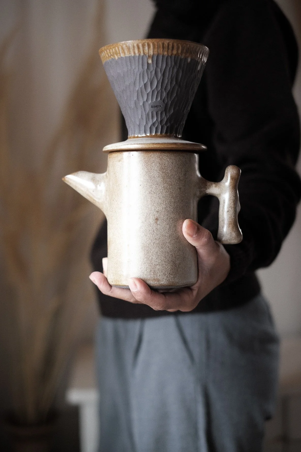 A person holding a ceramic pour-over coffee maker with a glass cone-shaped dripper on top.