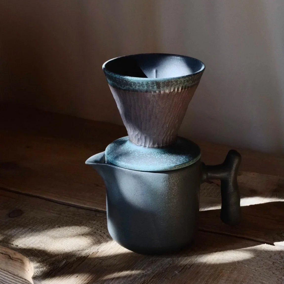 Person holding a textured black ceramic bowl, with three other textured ceramic bowls on a wooden surface in the background.