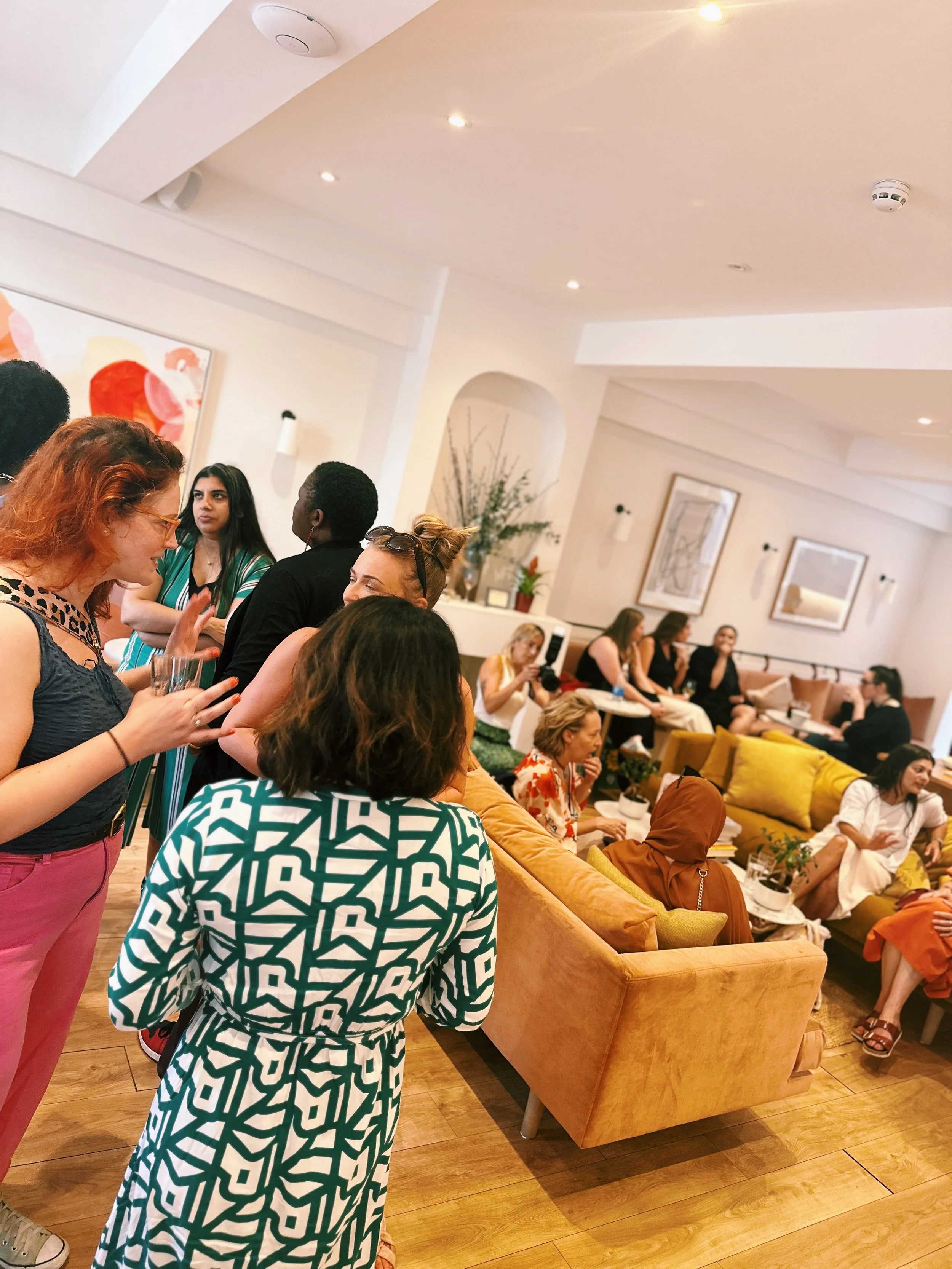 Group of diverse women socializing in a modern, cozy living room with yellow sofas and framed artwork on the walls.