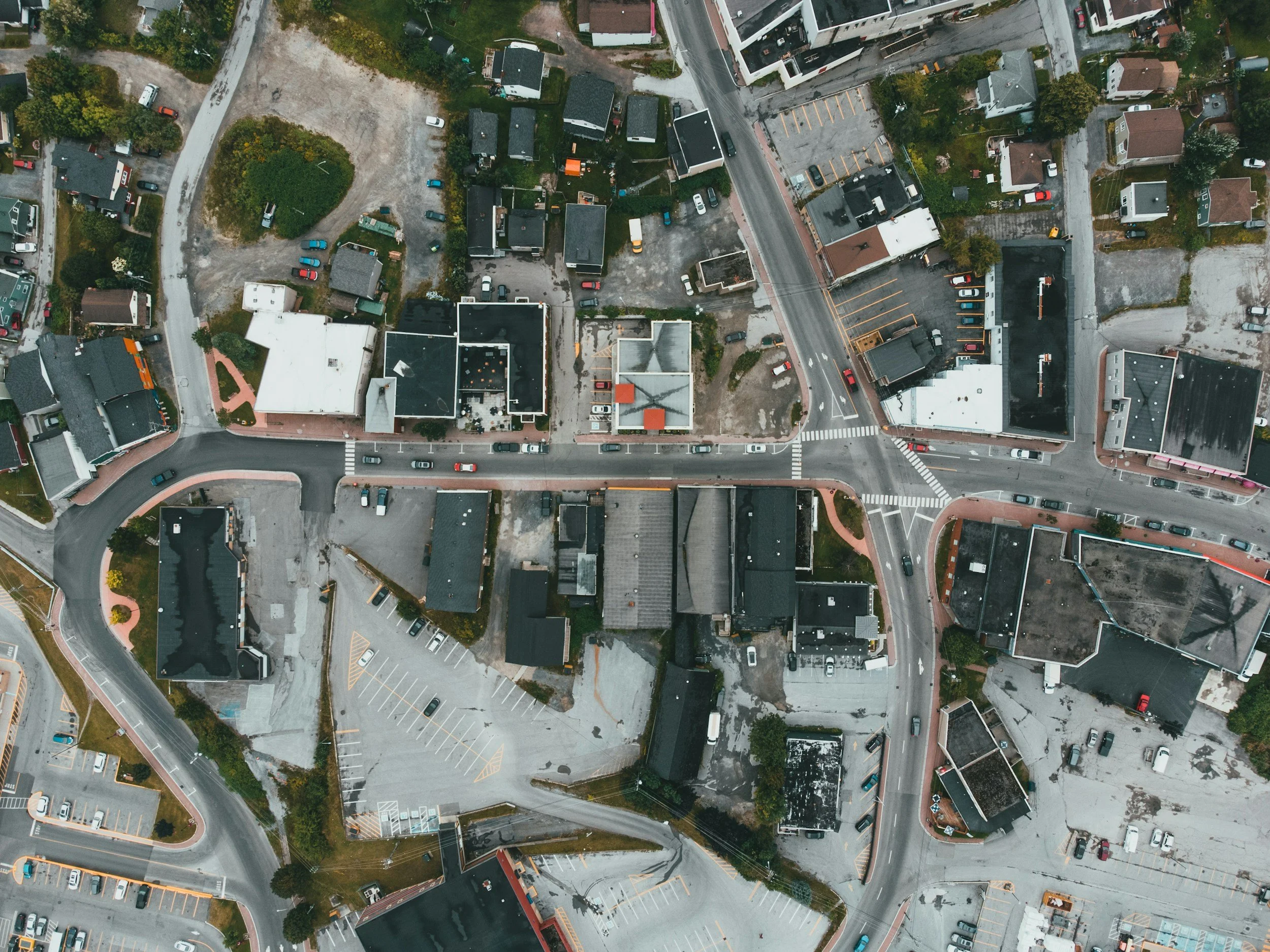 Aerial view of a city block with a mix of residential and commercial buildings, parking lots, and roads.