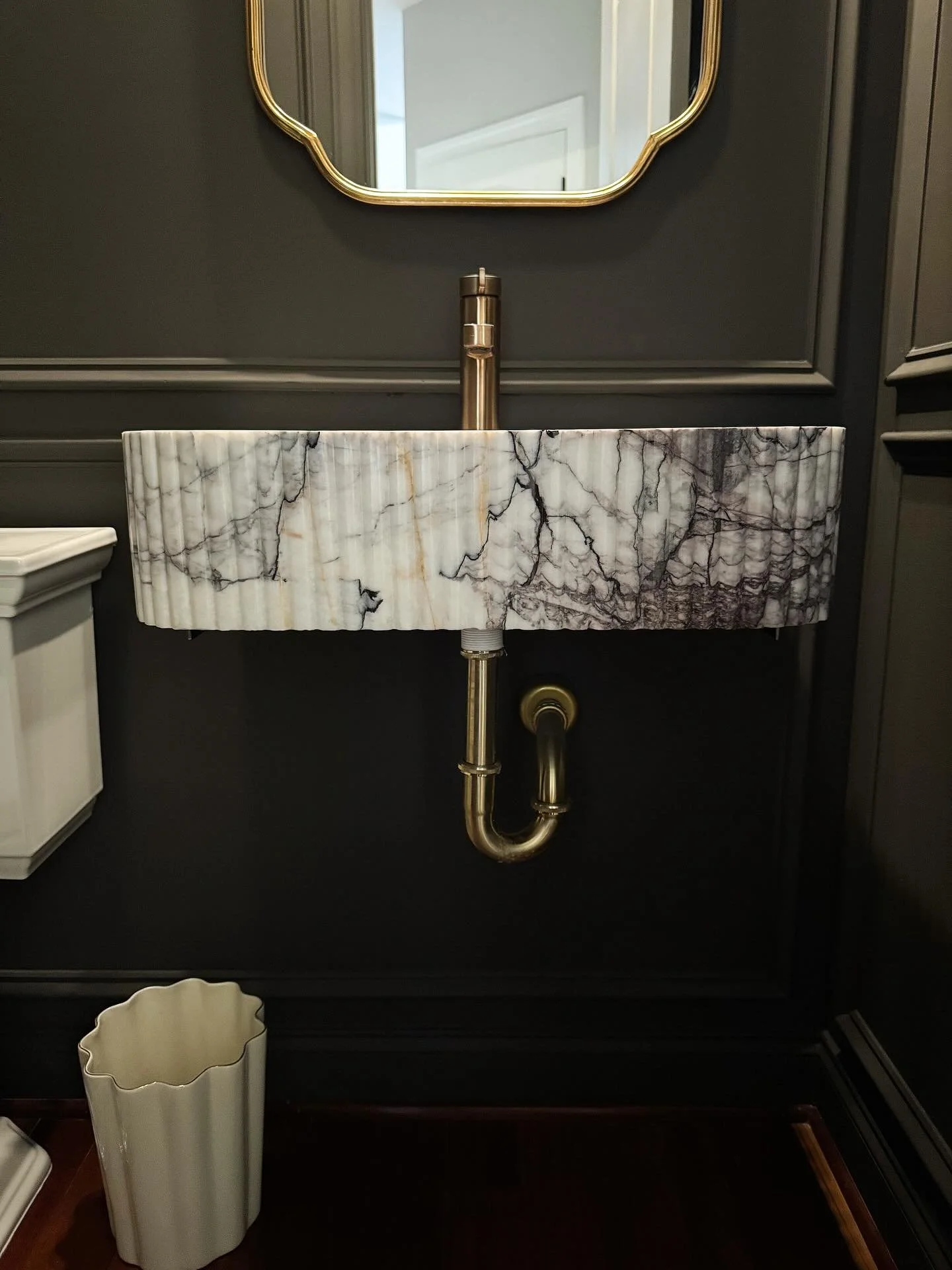 Small space, rich mood. 

Wrapped in urbane bronze and anchored by a custom marble sink sourced from Turkey, this little room brings the drama &mdash; in the best way. Every detail, from the glow of vintage brass to the quiet elegance of the molding,