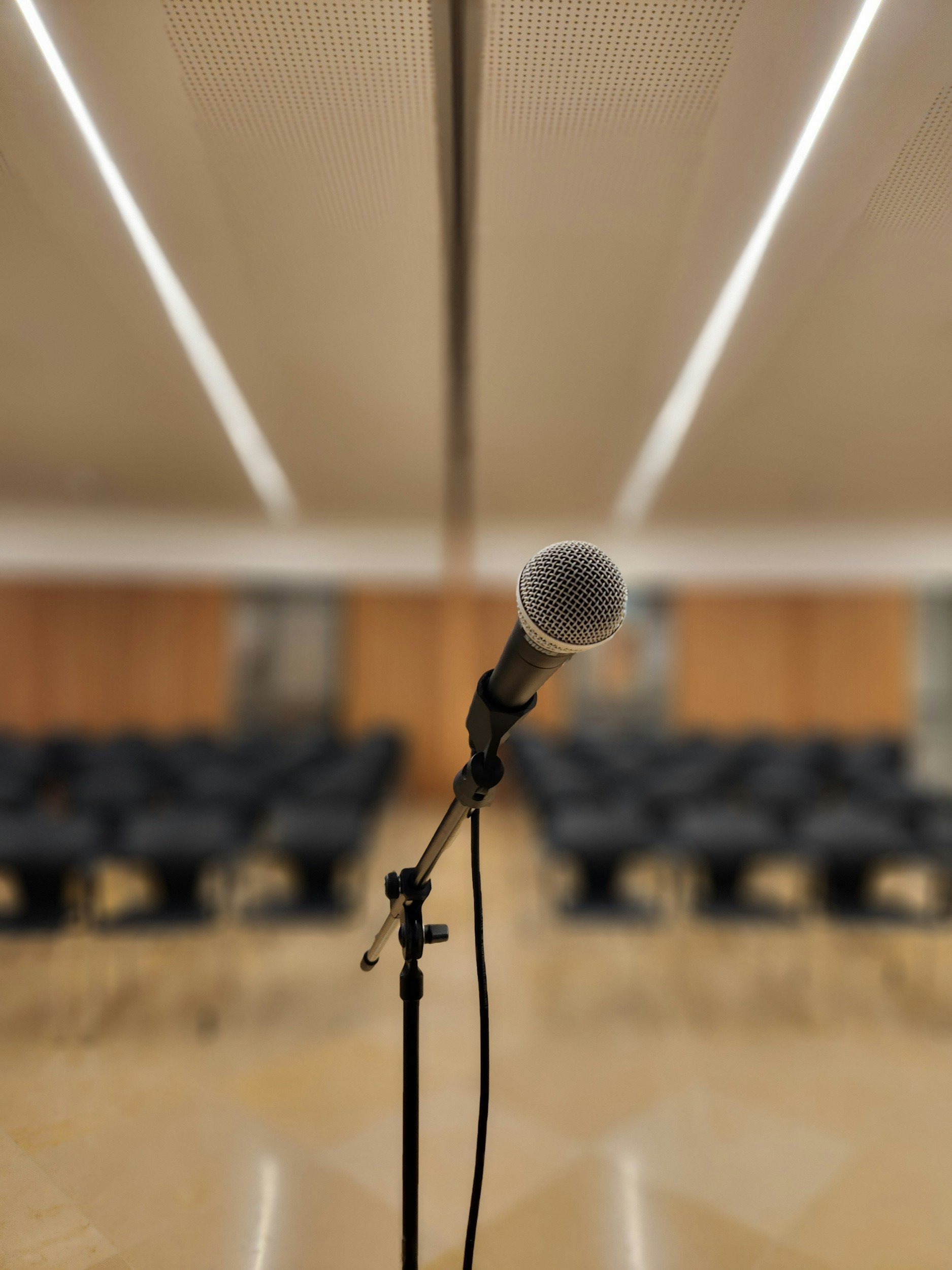 Microphone set up on stand in front of empty chairs in an auditorium or conference room.