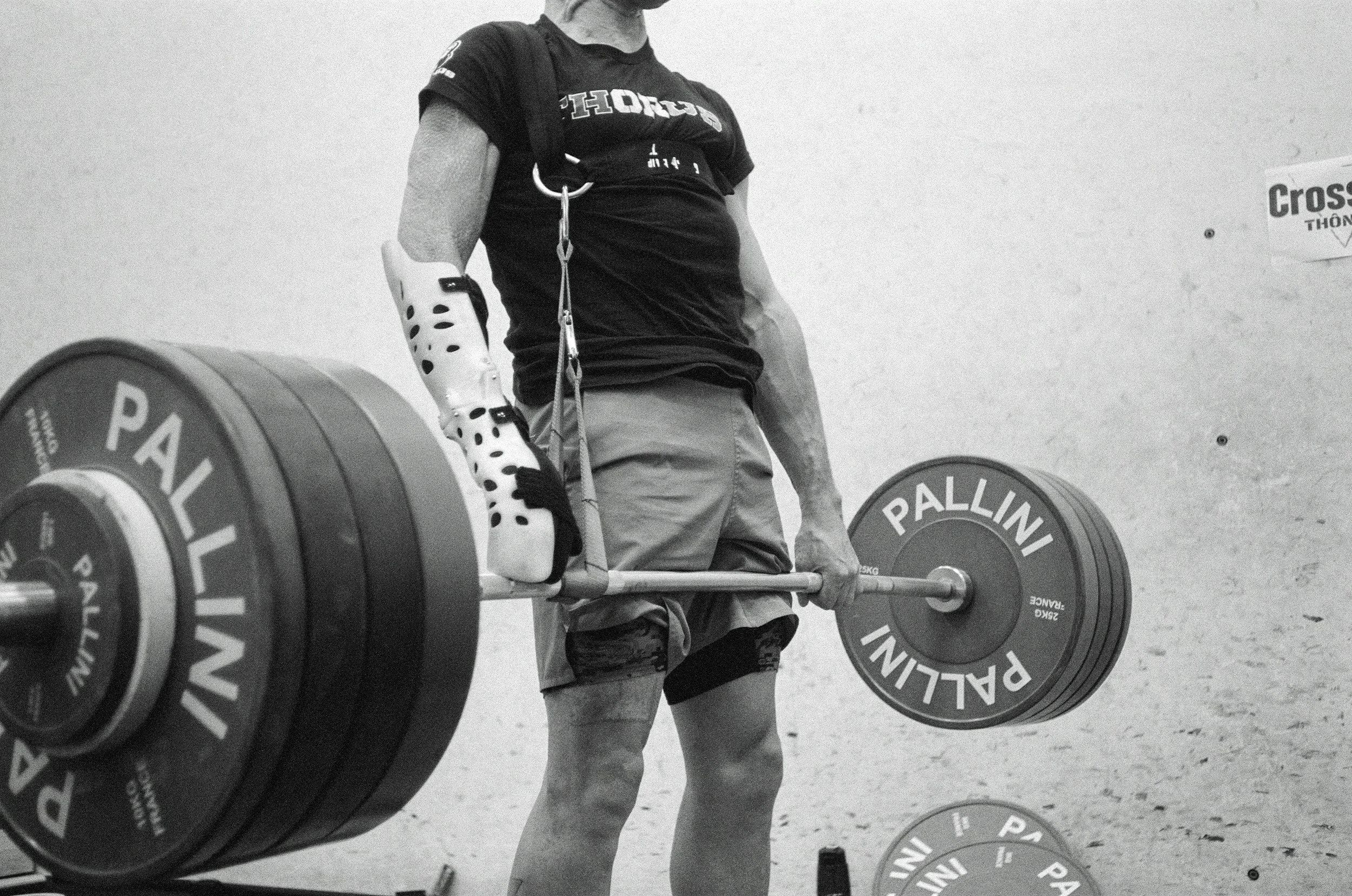 A person during weightlifting training, lifting a heavy barbell with large weight plates labeled 'PALLINI' in a gym or training facility.