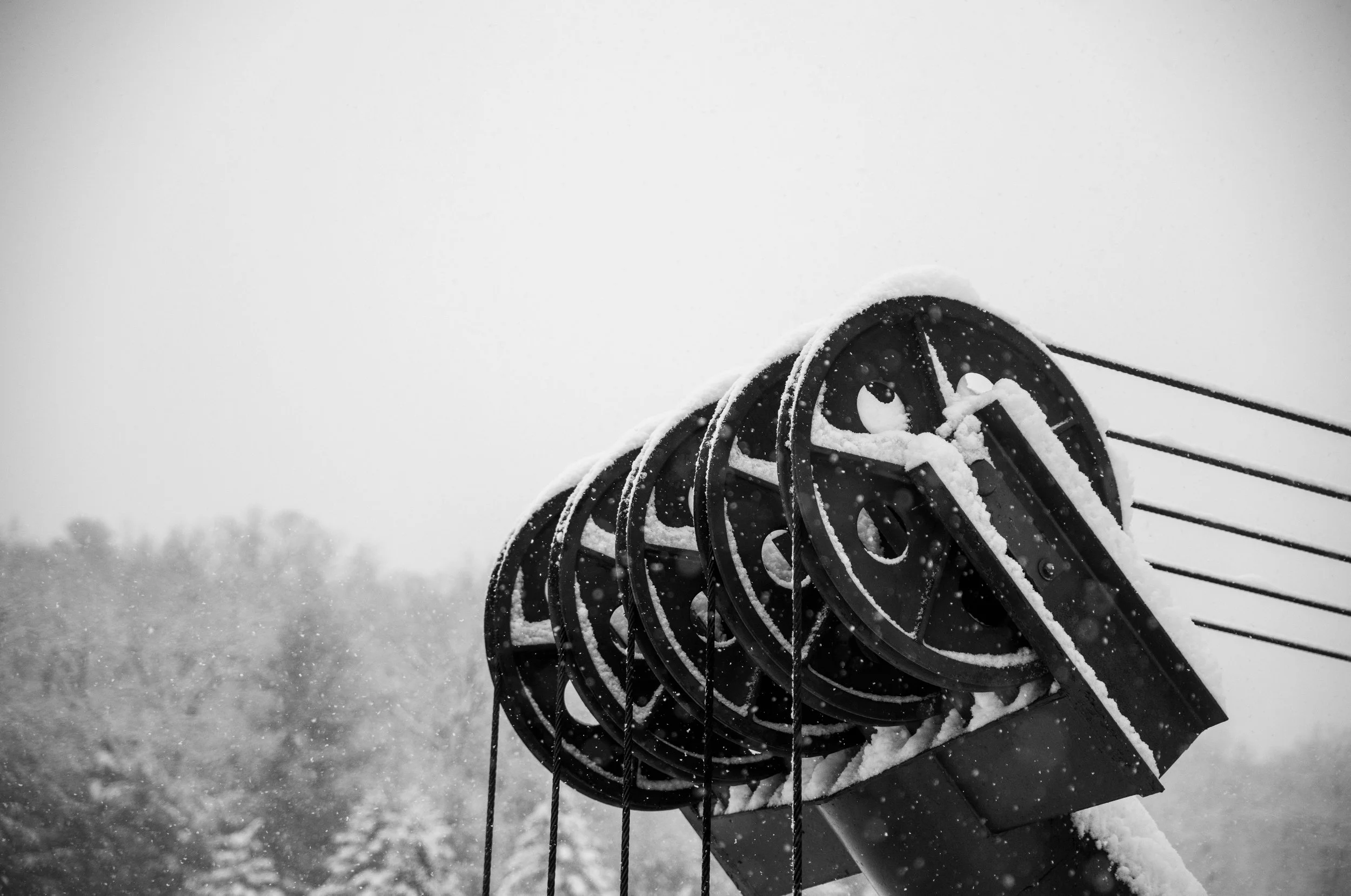 Snow-covered ski lift pulleys and cables on a snowy day.