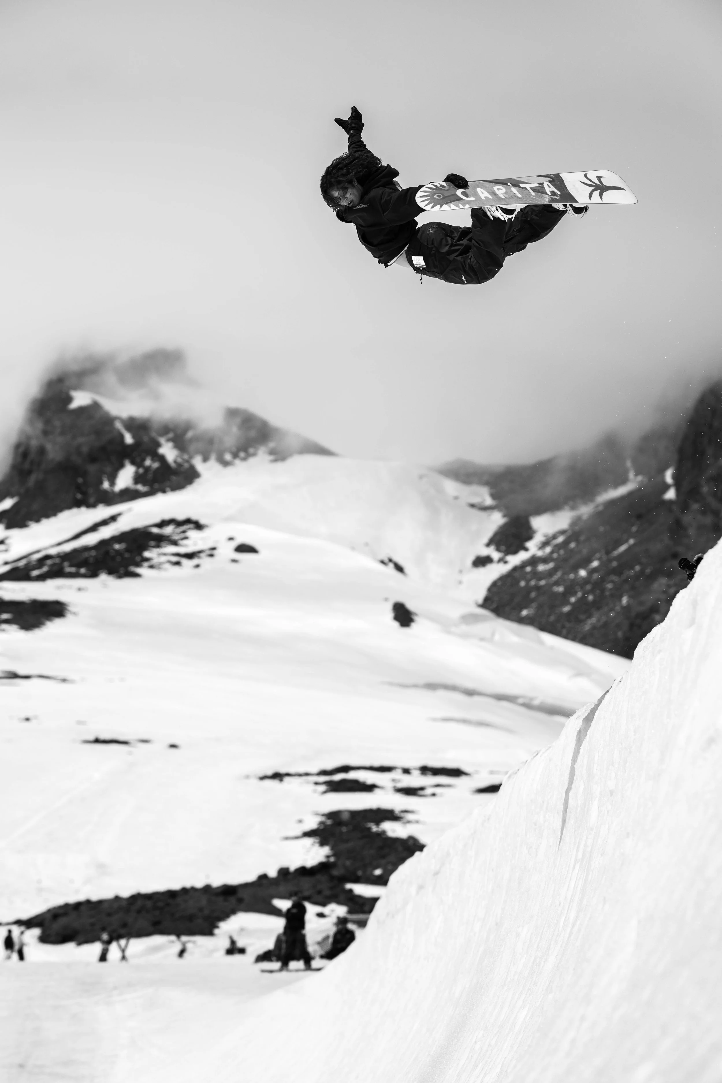 A person performing a snowboarding jump in a snowy mountain landscape in black and white.