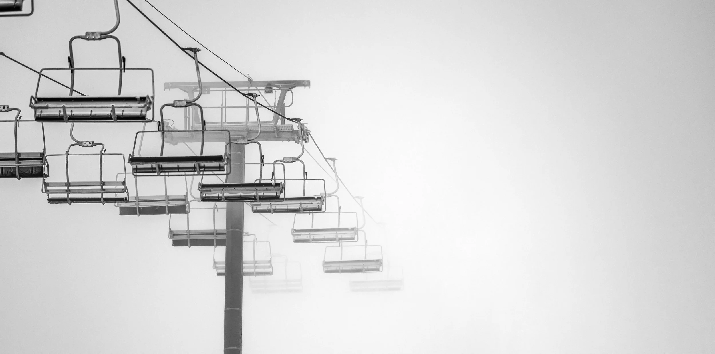Empty ski lift chairs suspended in foggy mountain landscape