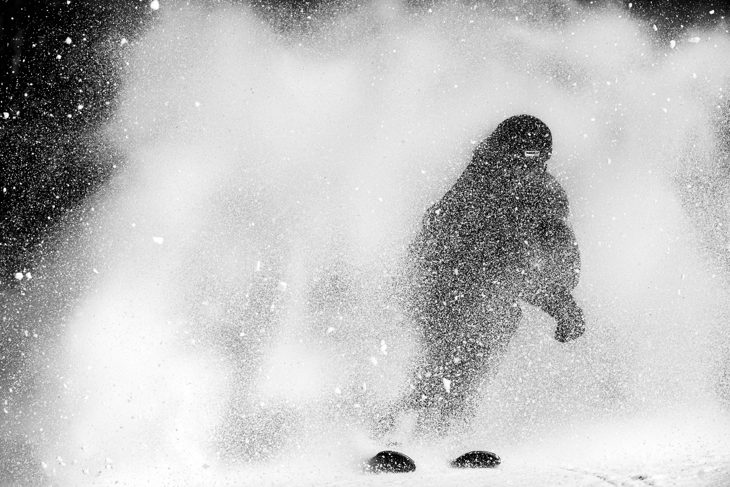 Person playing in the snow, bundled in winter clothing, with snow flying around.