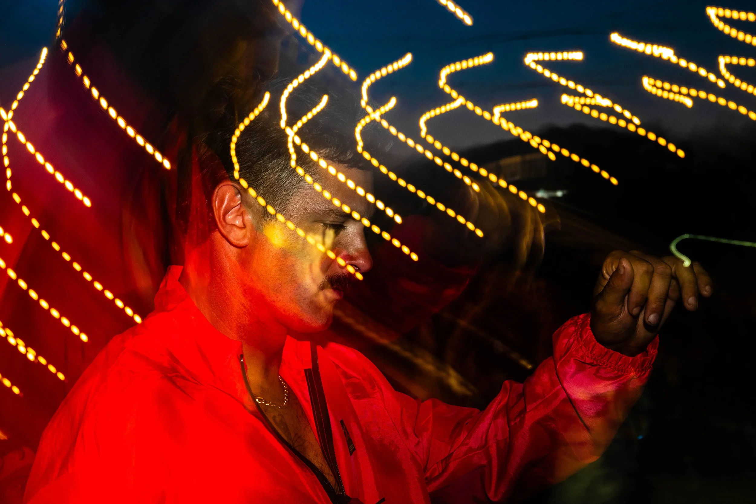 A man in a red jacket with closed eyes, engaging with light trails in a dark setting, creating a motion blur effect.