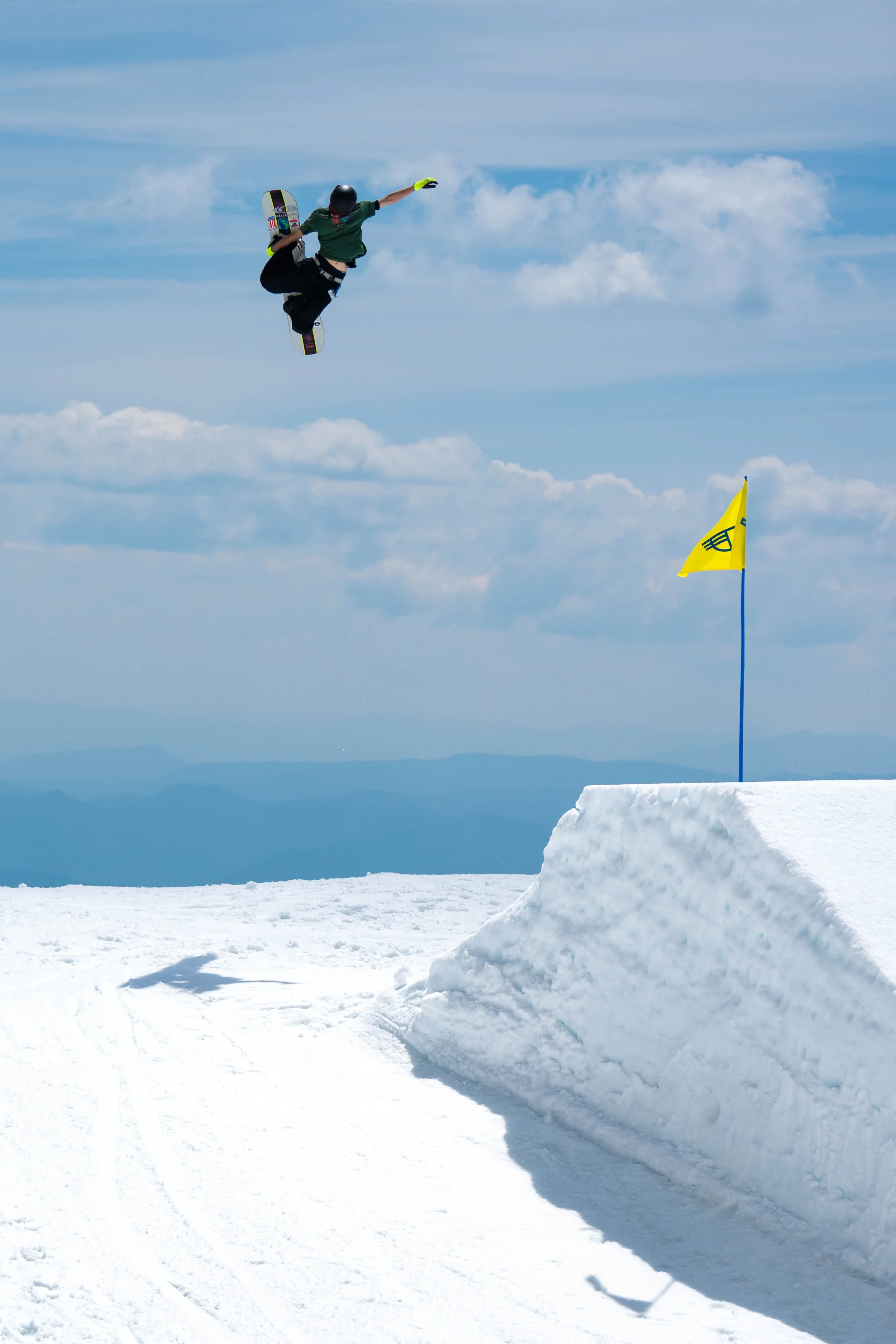 A snowboarder in mid-air performing a jump against a snowy mountain landscape and partly cloudy sky.