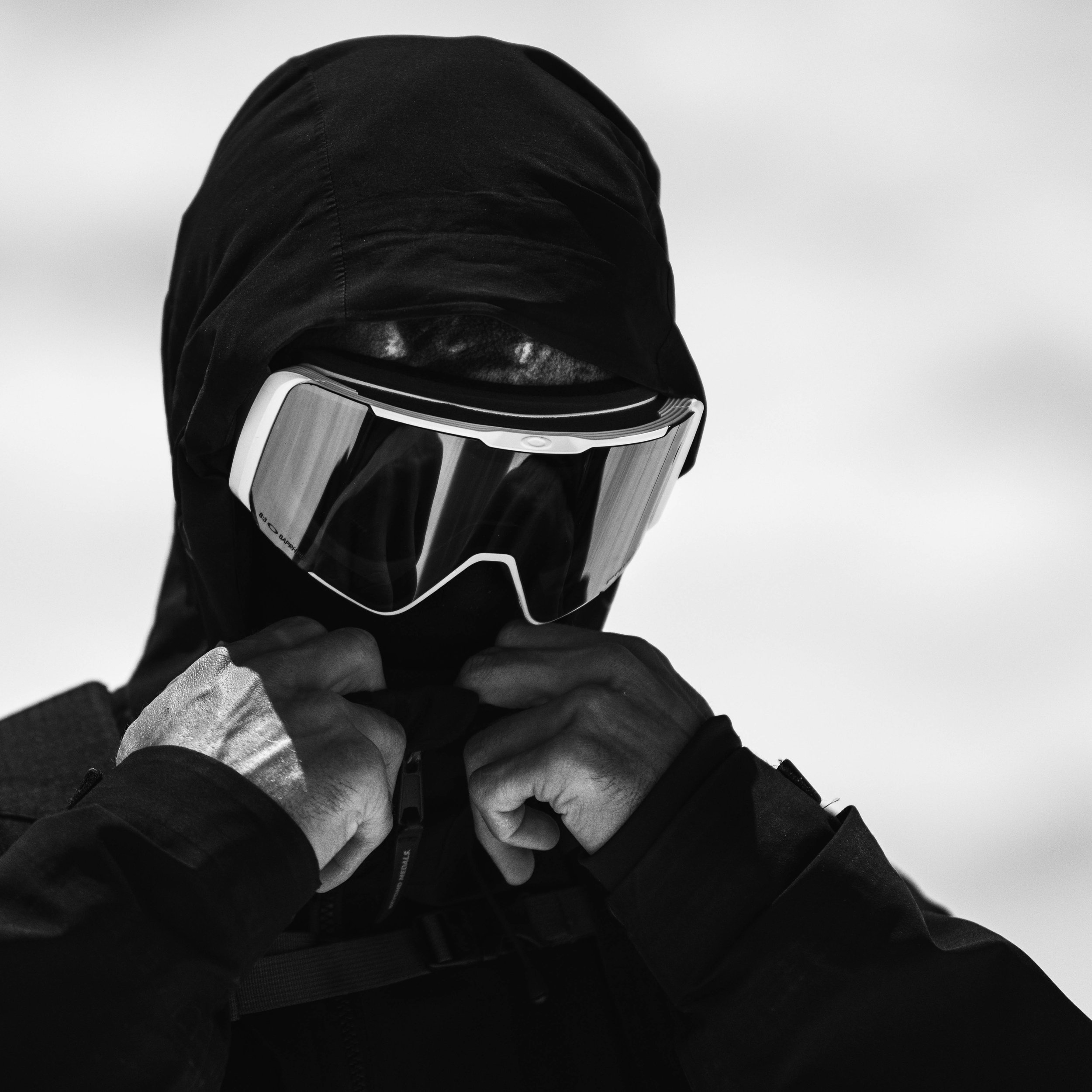 Person wearing black hooded jacket and goggles, adjusting their jacket.