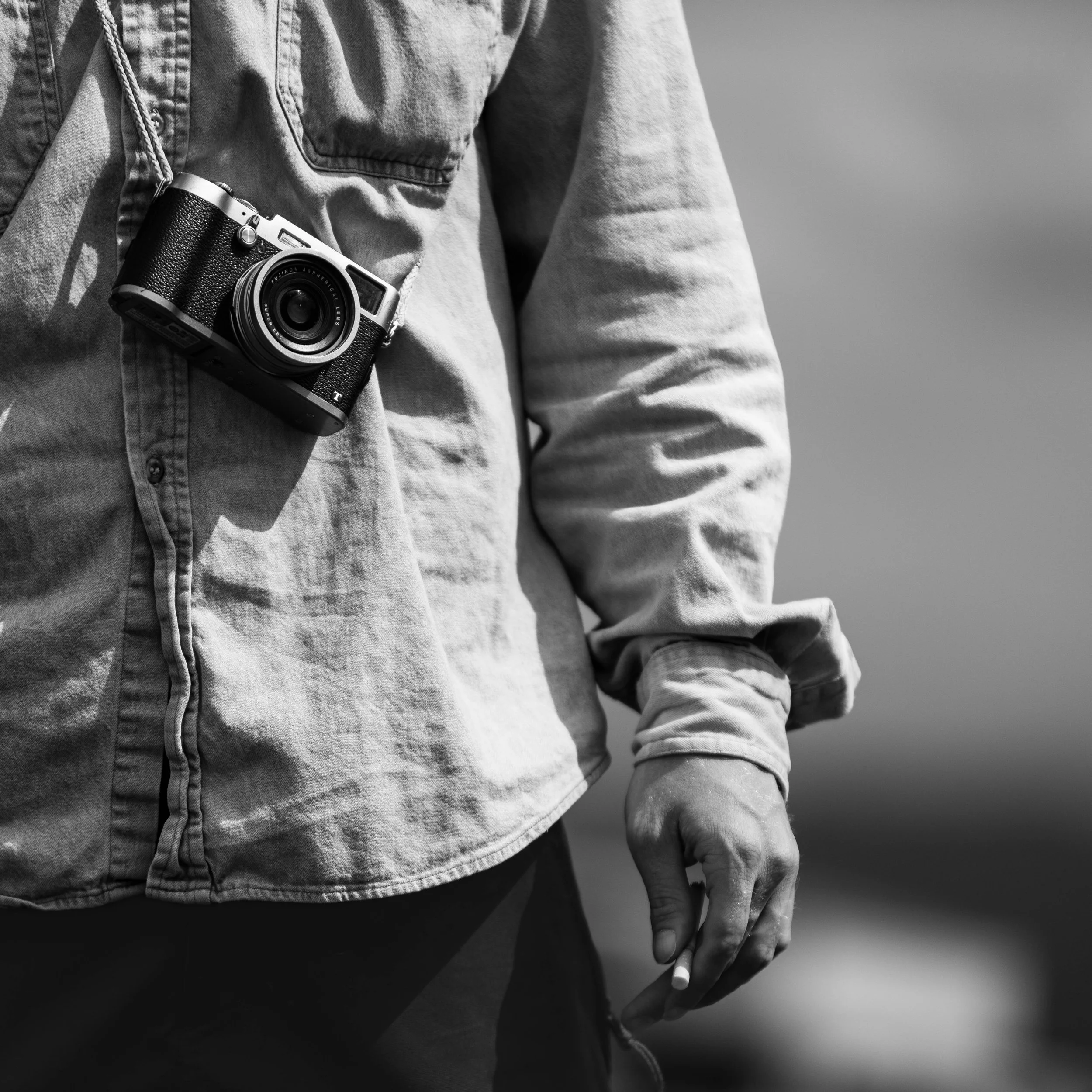 A person wearing a denim shirt with a camera hanging around their neck in black and white.
