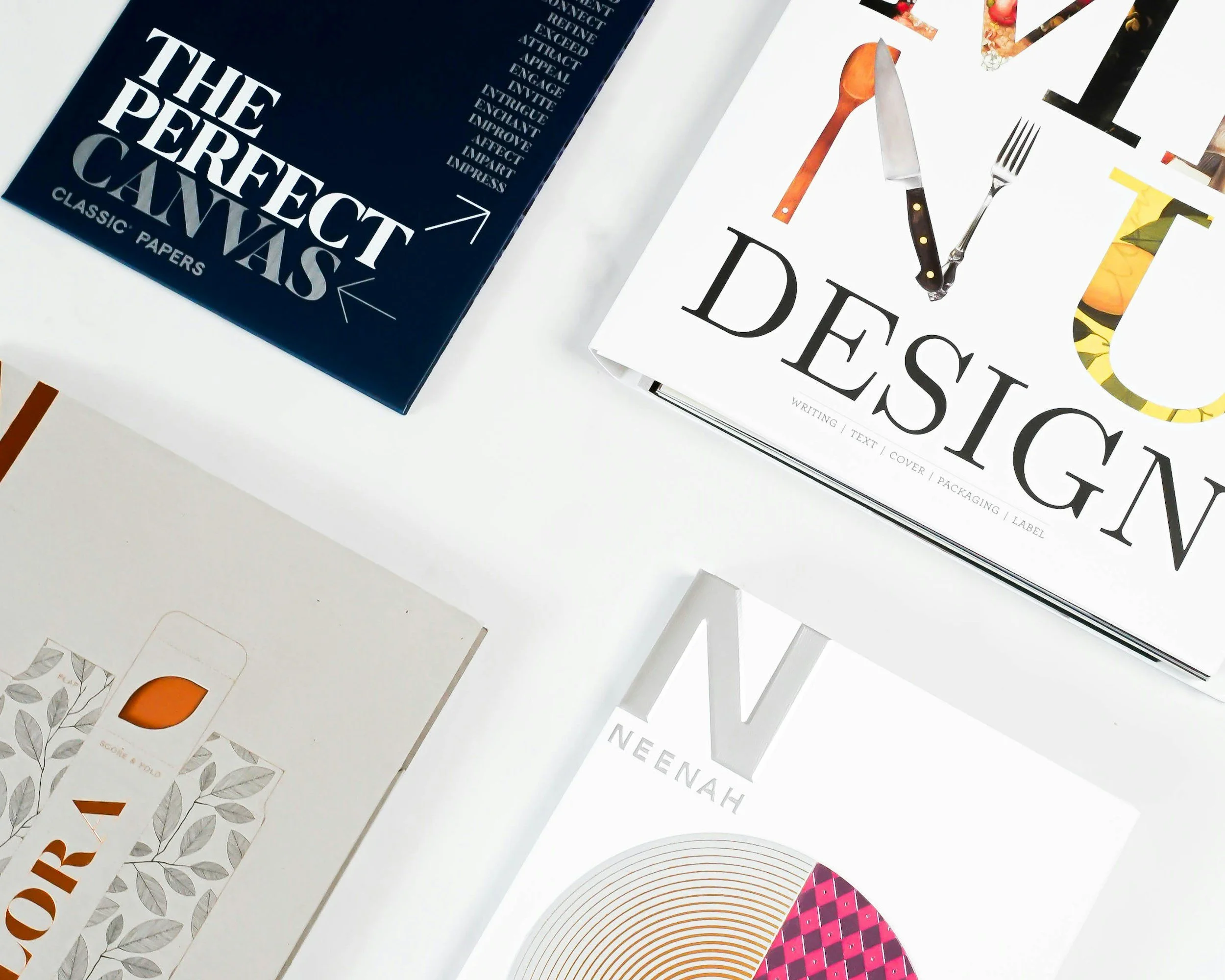Top-down view of various design and art books, including titles about the perfect canvas, design, and a book with a colorful circular pattern on the cover, laid out on a white surface.