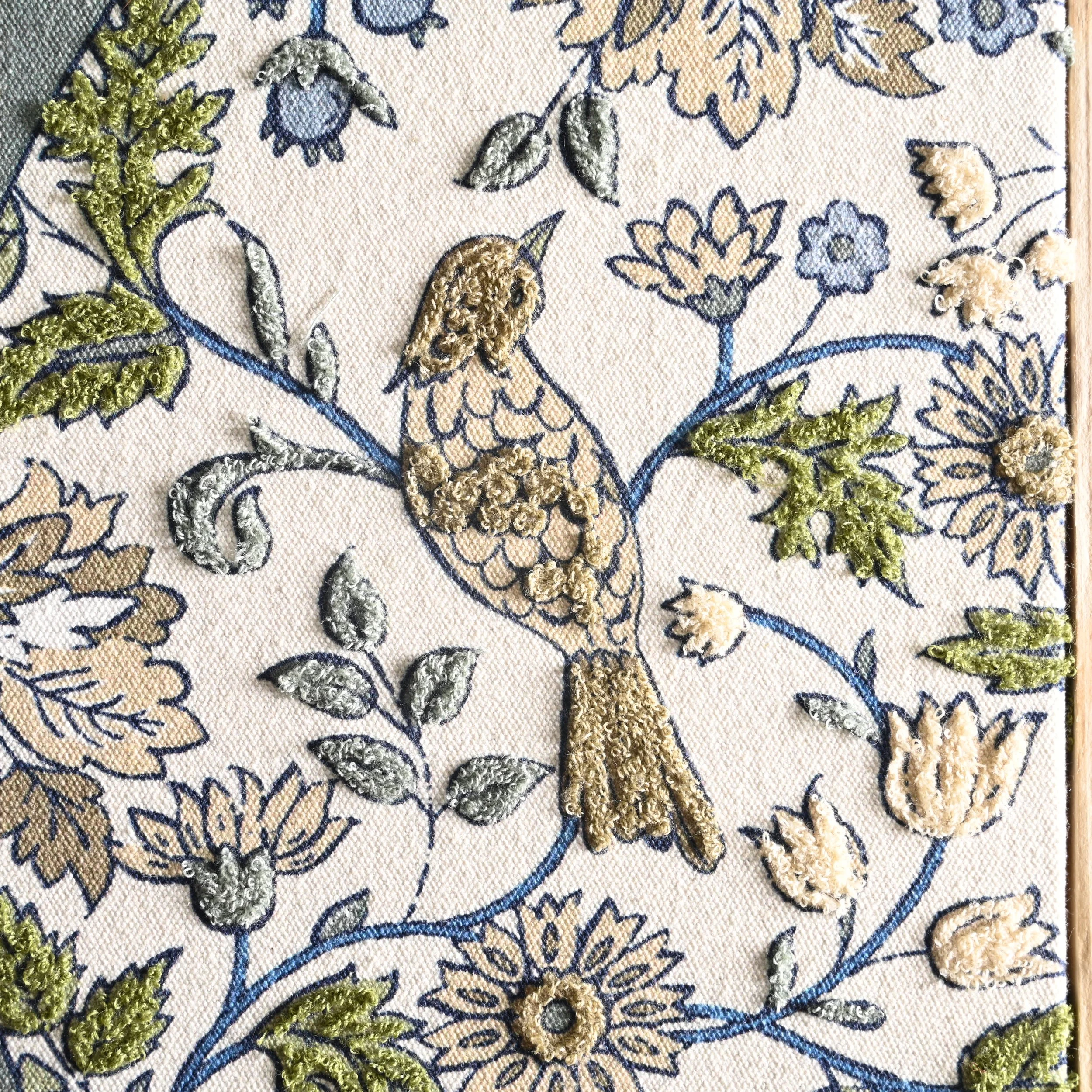Embroidery of a bird surrounded by flowers and leaves on fabric.