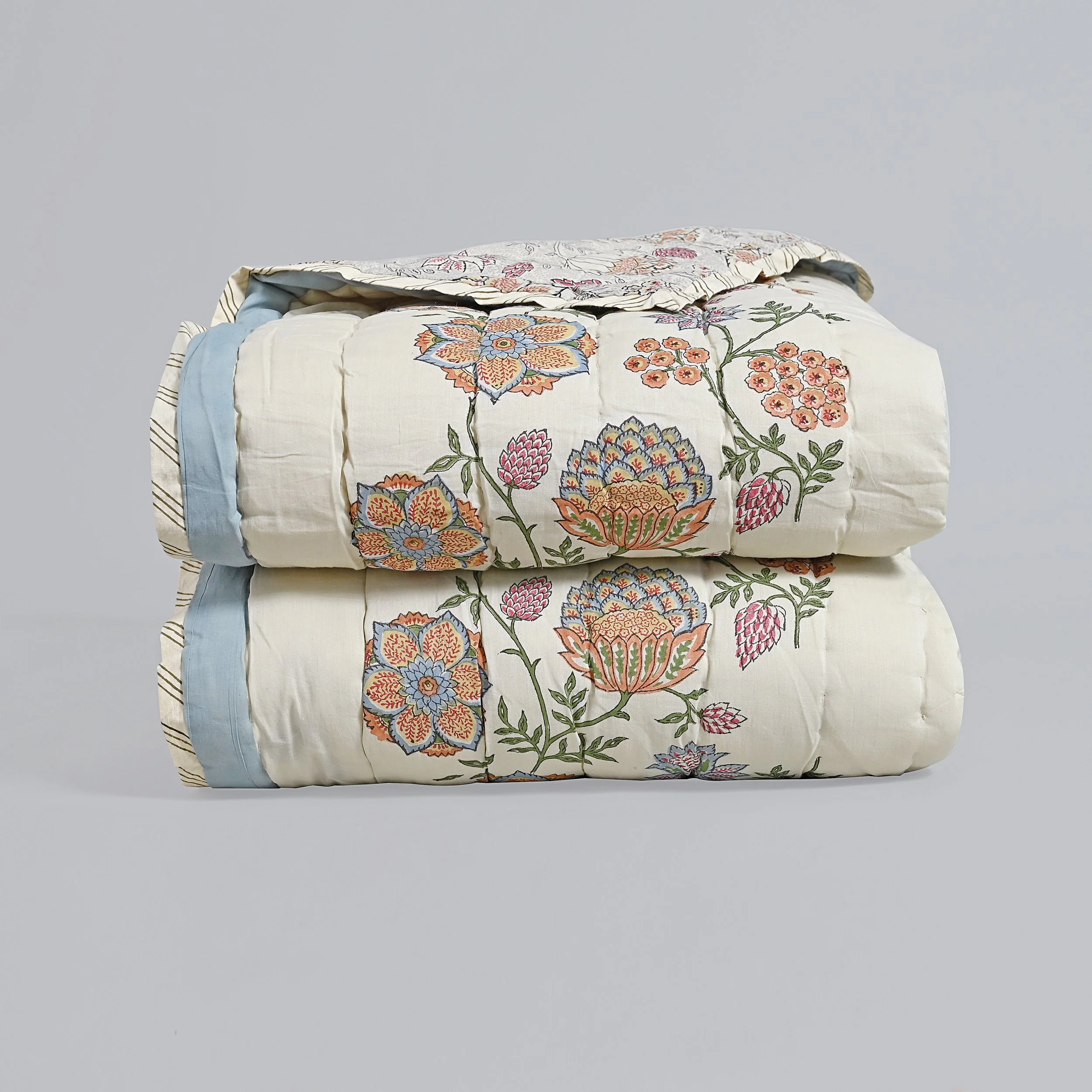 Stacked floral quilted blankets with embroidered flower patterns, one folded back to show the colorful design.