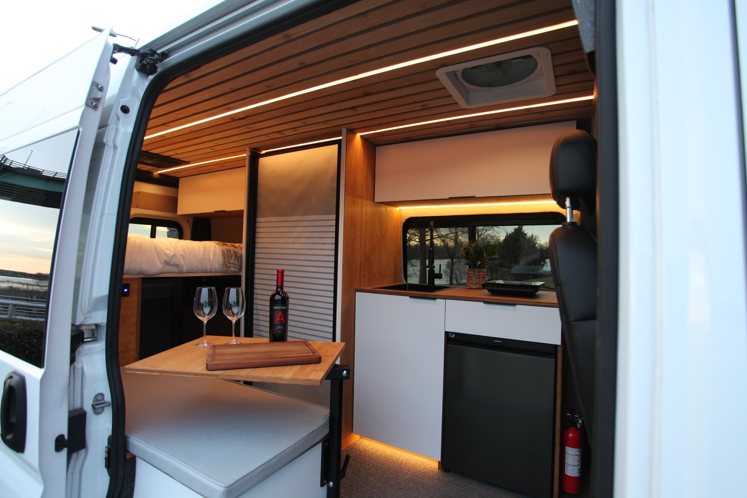 Off-grid camper van interior with bed platform, kitchen, storage cabinetry, and ambient lighting.
