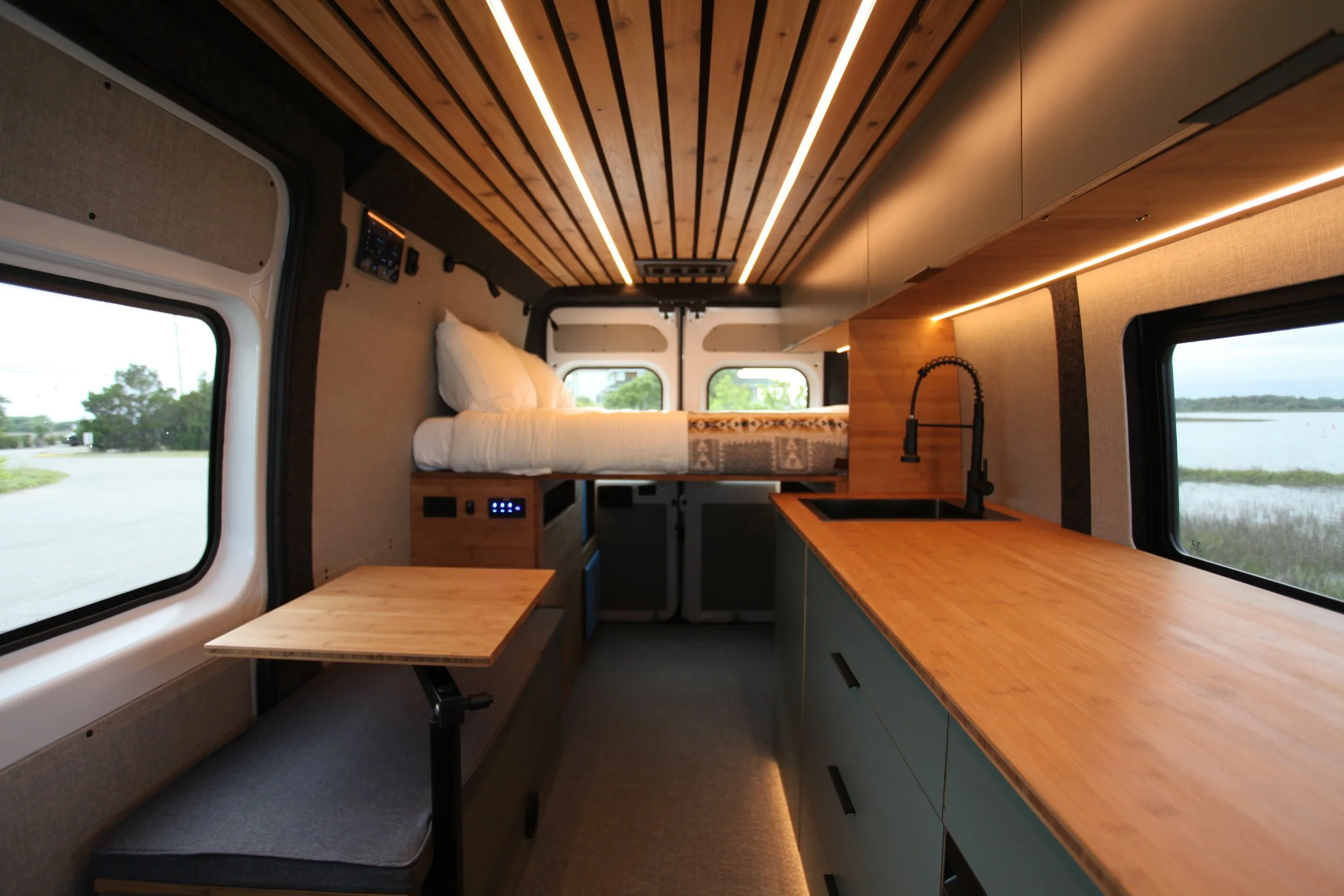 Luxury Ram Promaster camper van conversion featuring a rear bed, kitchen, and custom cabinetry.