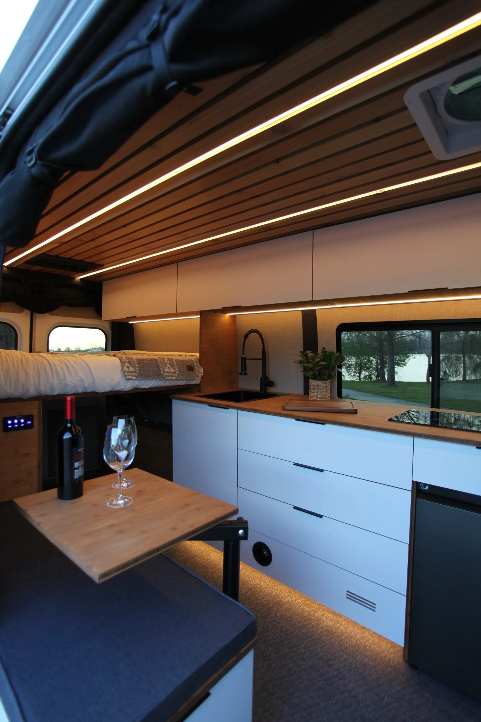 Custom camper van interior with galley kitchen, upper cabinetry, and panoramic windows by Vantra.