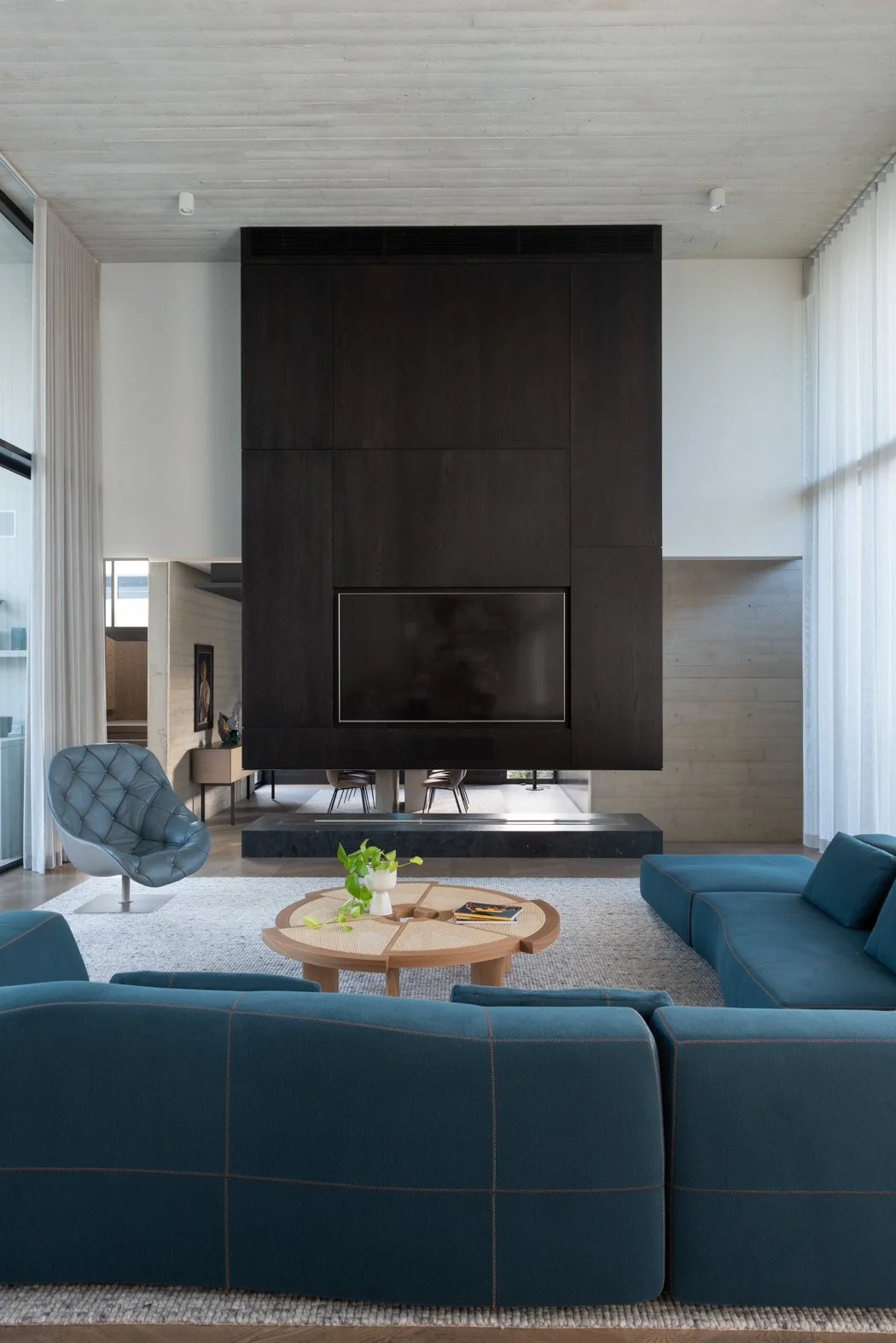 Modern living room with teal sectional sofa, round coffee table with decorations, blue armchair, and a large black fireplace with TV.