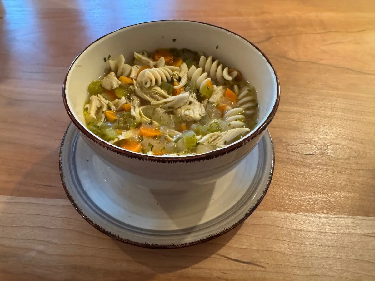 Bowl of gluten-free chicken noodle soup with shredded chicken, carrots, celery, and spiral pasta on a wooden table
