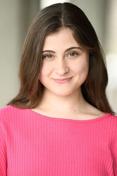 Portrait of a young woman with long brown hair, wearing a pink top, smiling softly.