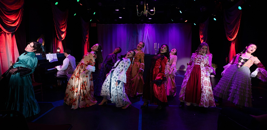 The image shows a stage with performers in vintage costumes, some singing and others playing the piano, under purple and red lighting, with red curtains and a chandelier overhead.