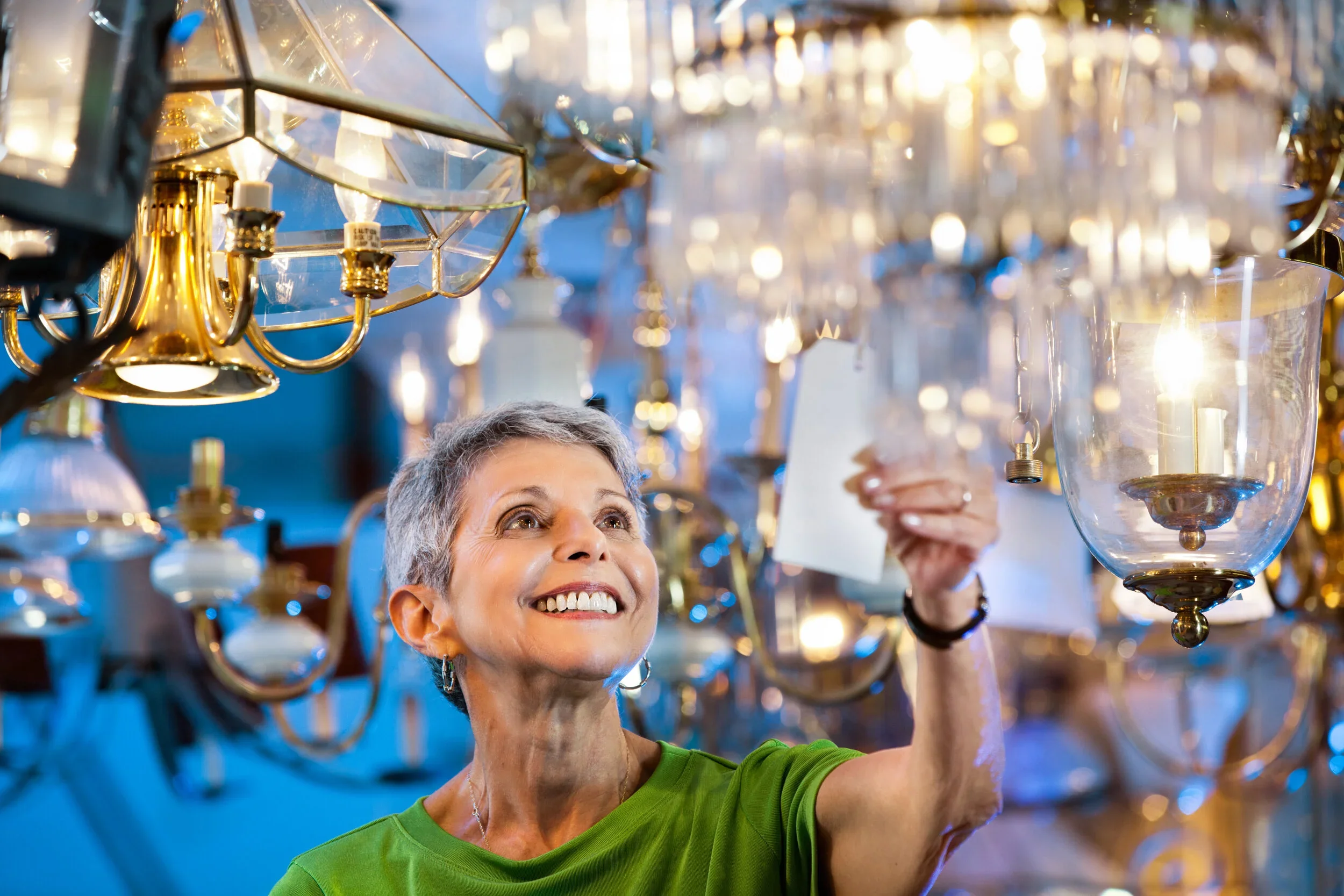 A woman with short gray hair and a green shirt examining a chandelier at the ReStore.
