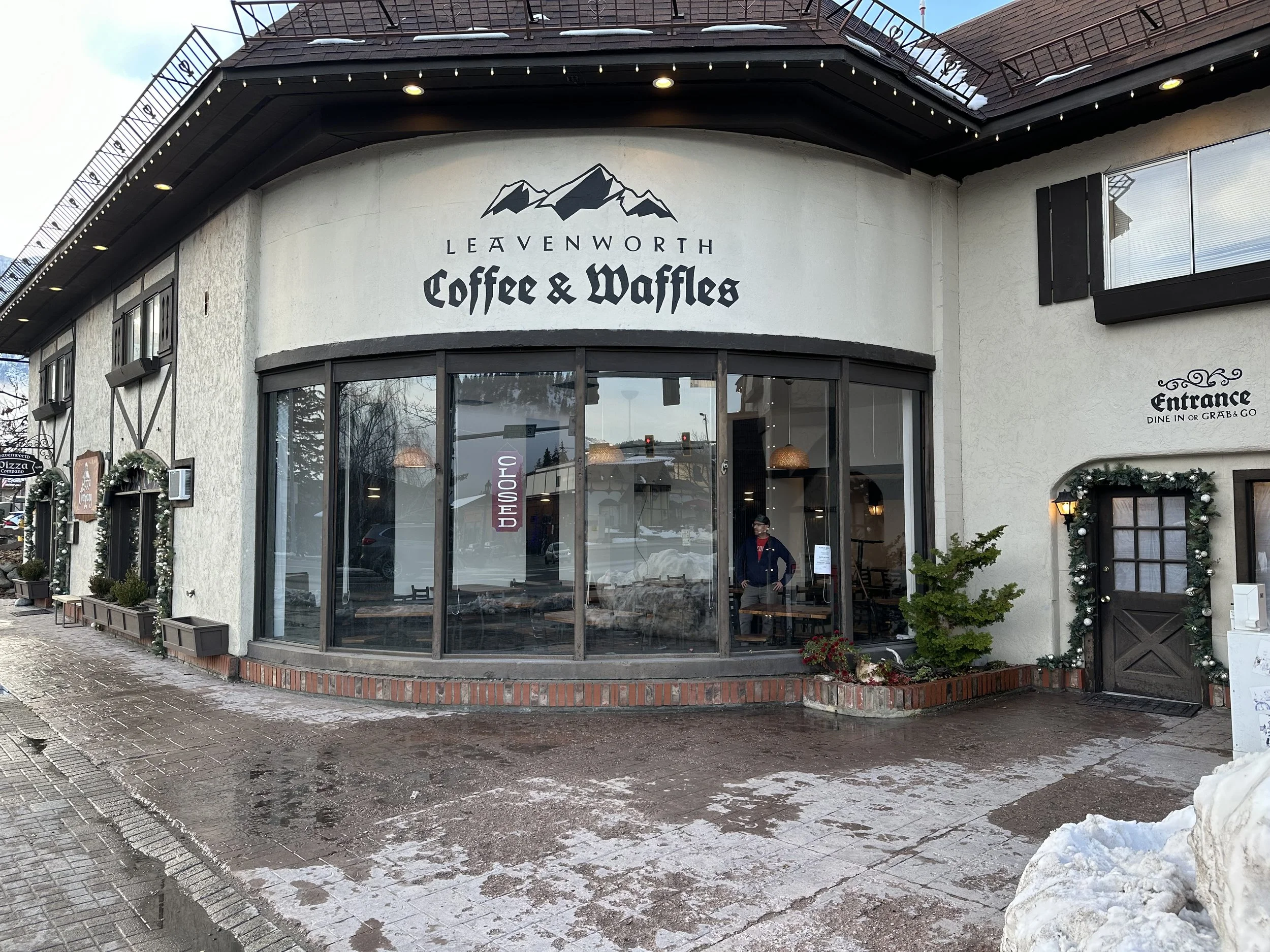 Exterior view of Leavenworth Coffee & Waffles restaurant with large windows and a sign, decorated with Christmas garlands, on a cloudy winter day.