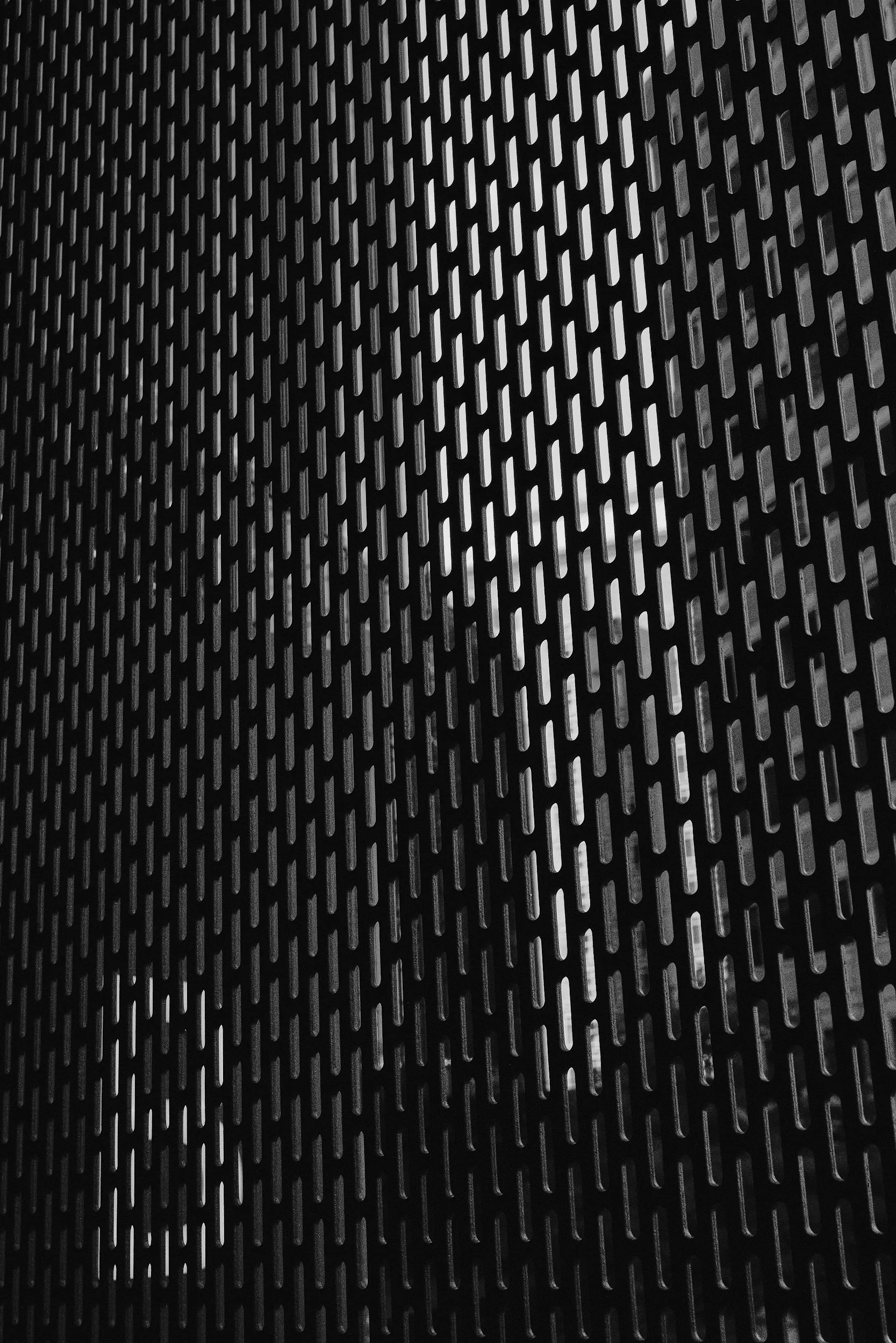 Close-up of a black metal surface with a repeating pattern of elongated oval holes.