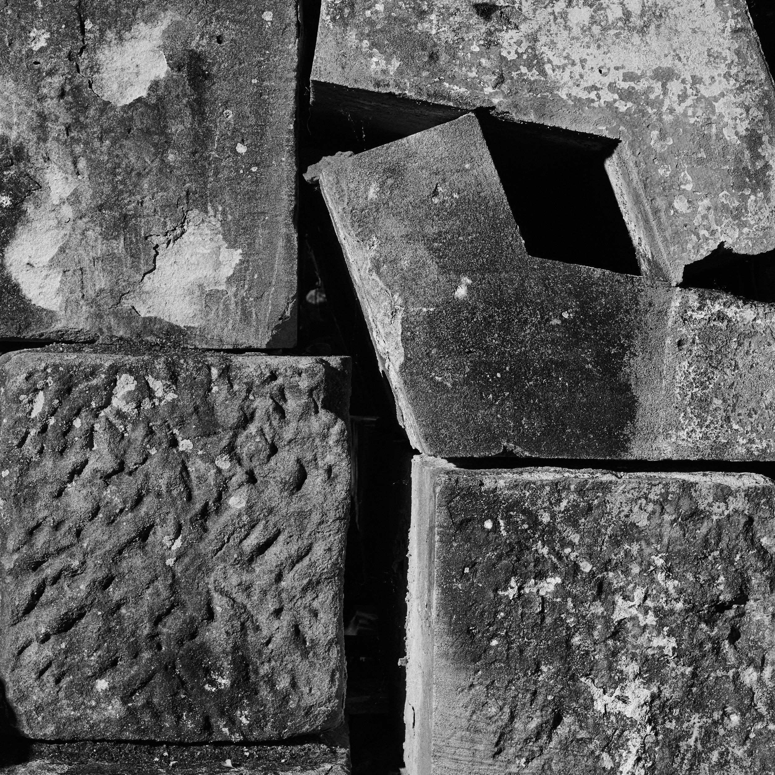 Close-up view of a stone wall with rough and uneven surface, showing various shades of gray and black, with some small patches of lichen or moss.