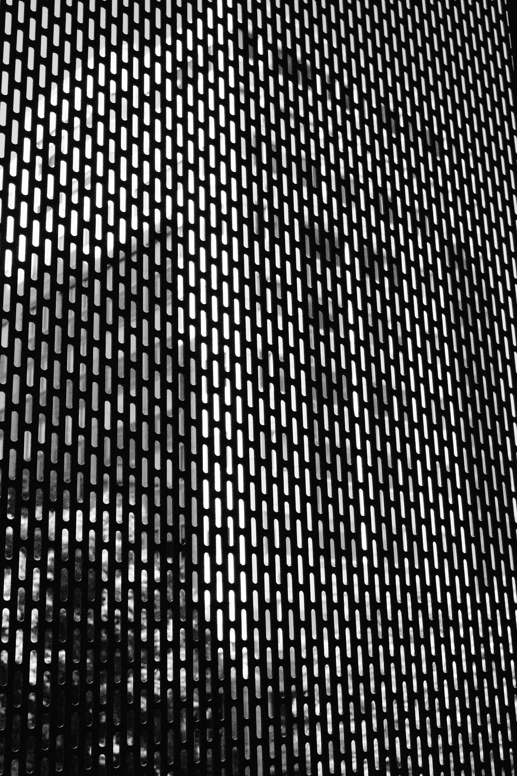 Close-up of a black metallic surface with elongated oval-shaped holes arranged in a regular pattern.