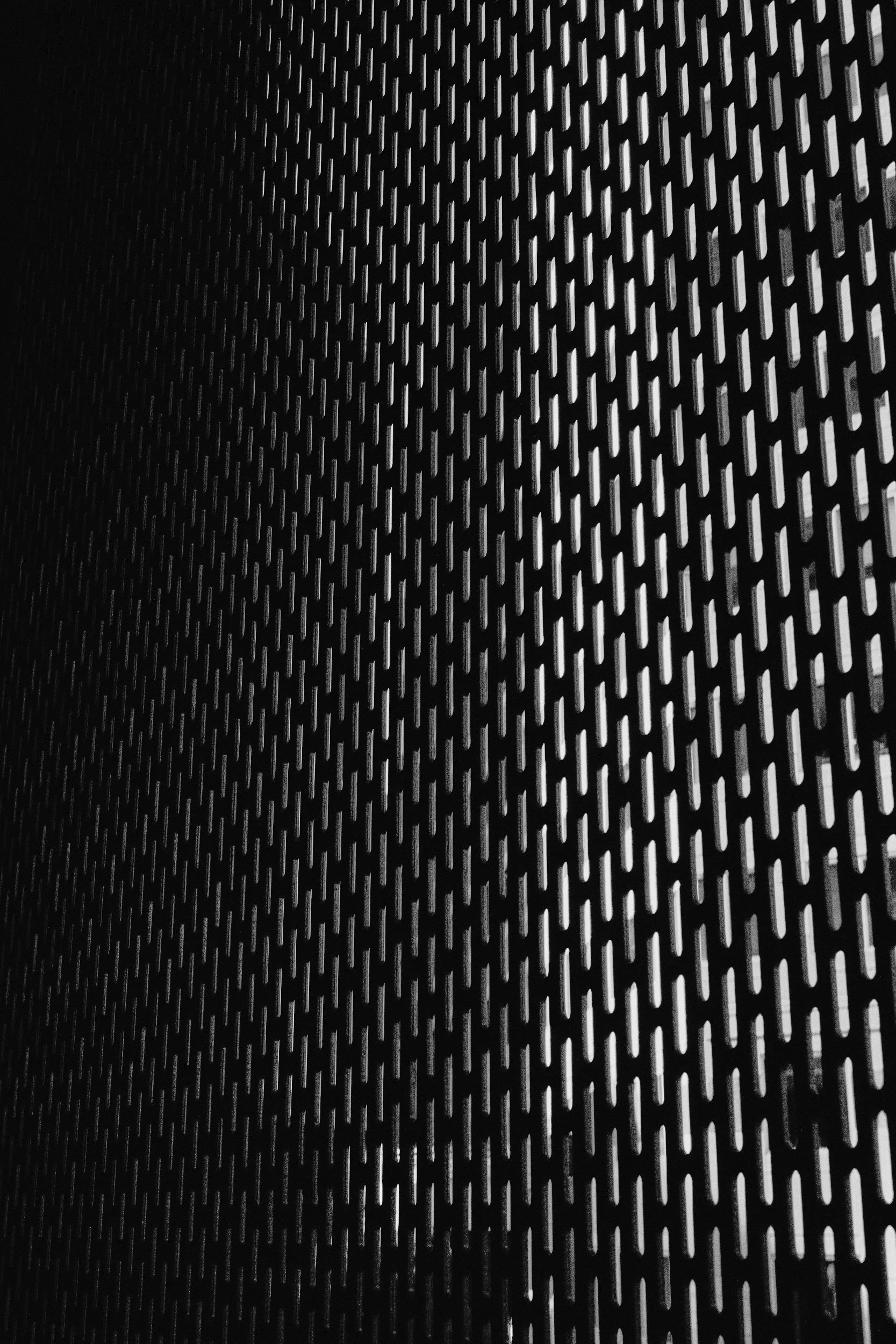 Close-up of black metal surface with evenly spaced elongated cutouts in a grid pattern.