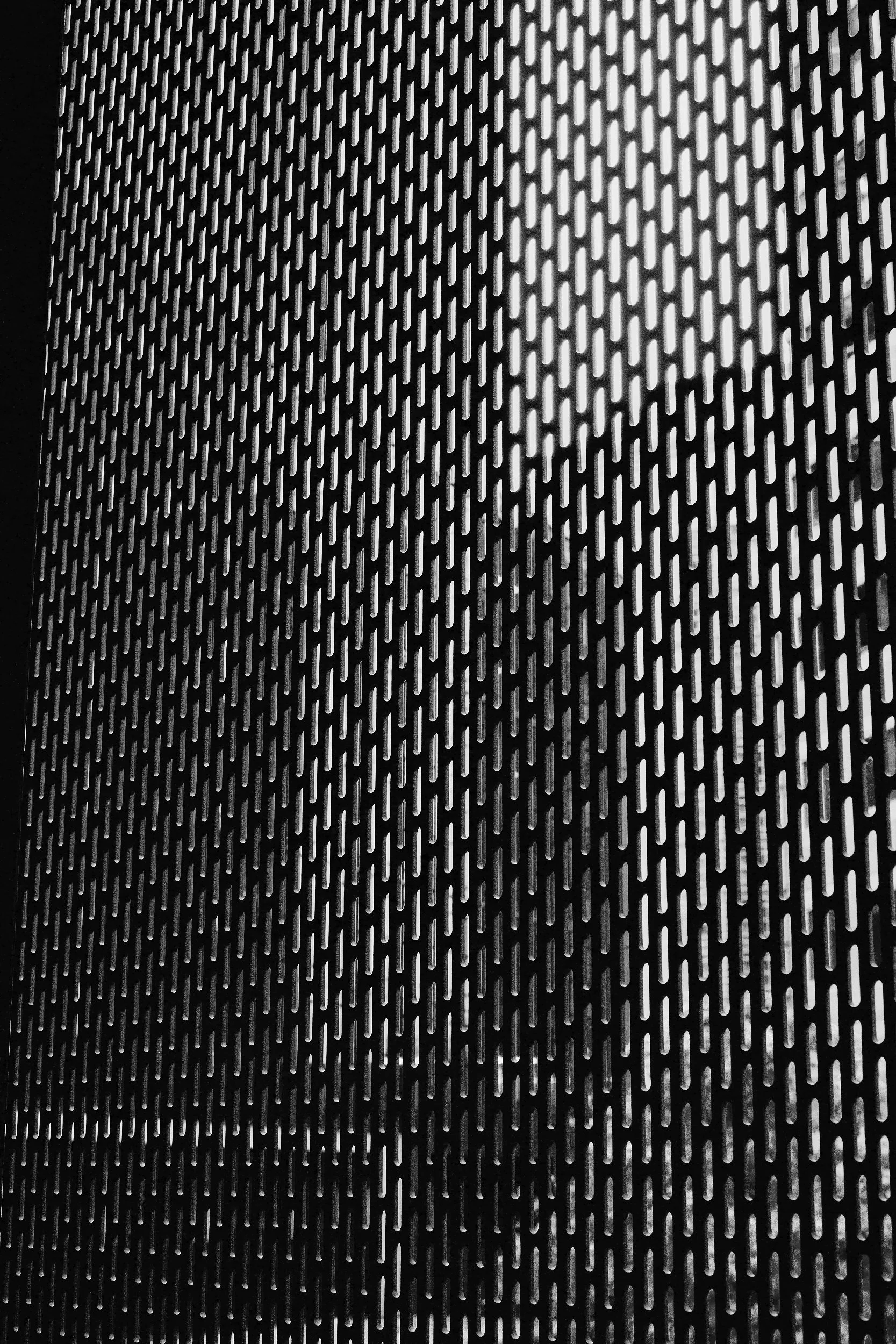 Black metal surface with evenly spaced elongated oval holes in a grid pattern.