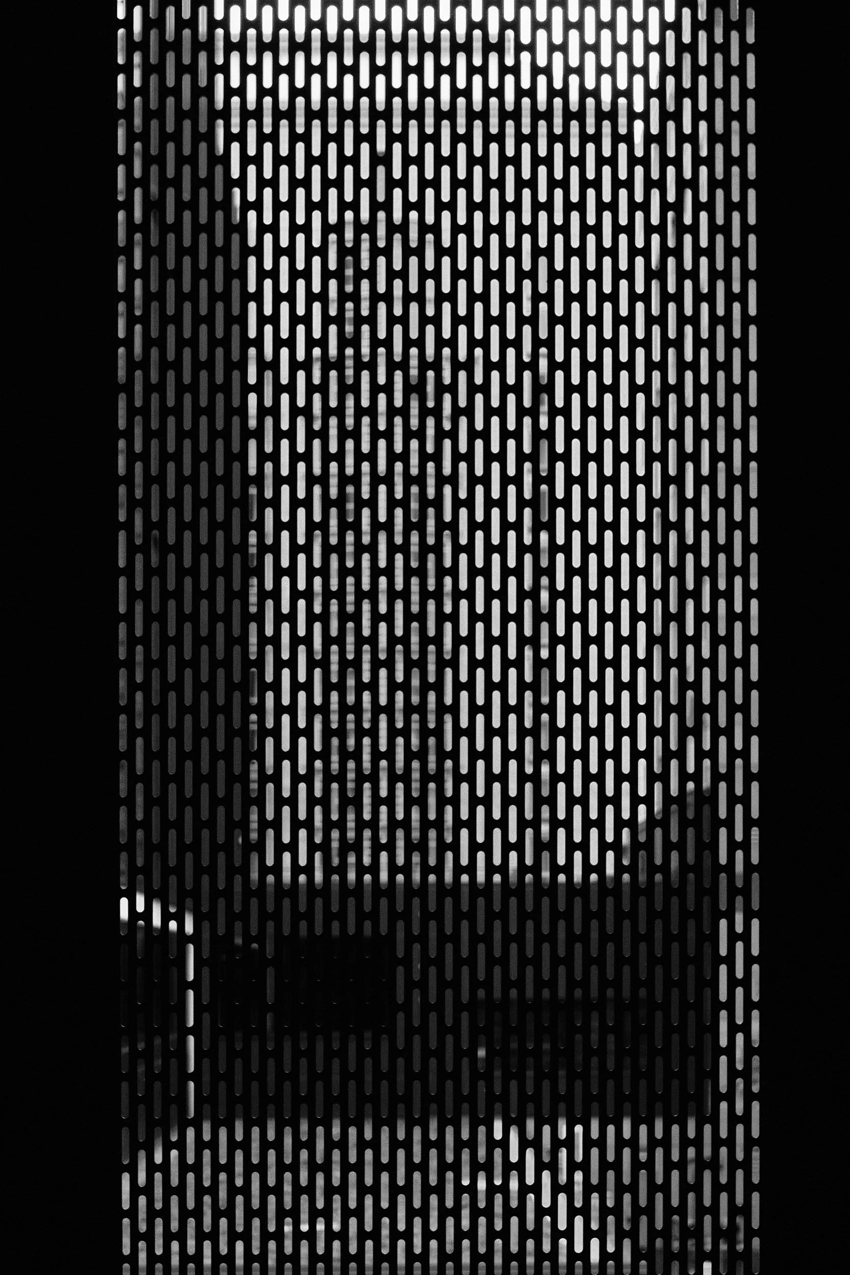 A close-up of a metallic surface with a pattern of elongated oval-shaped holes arranged in vertical rows.