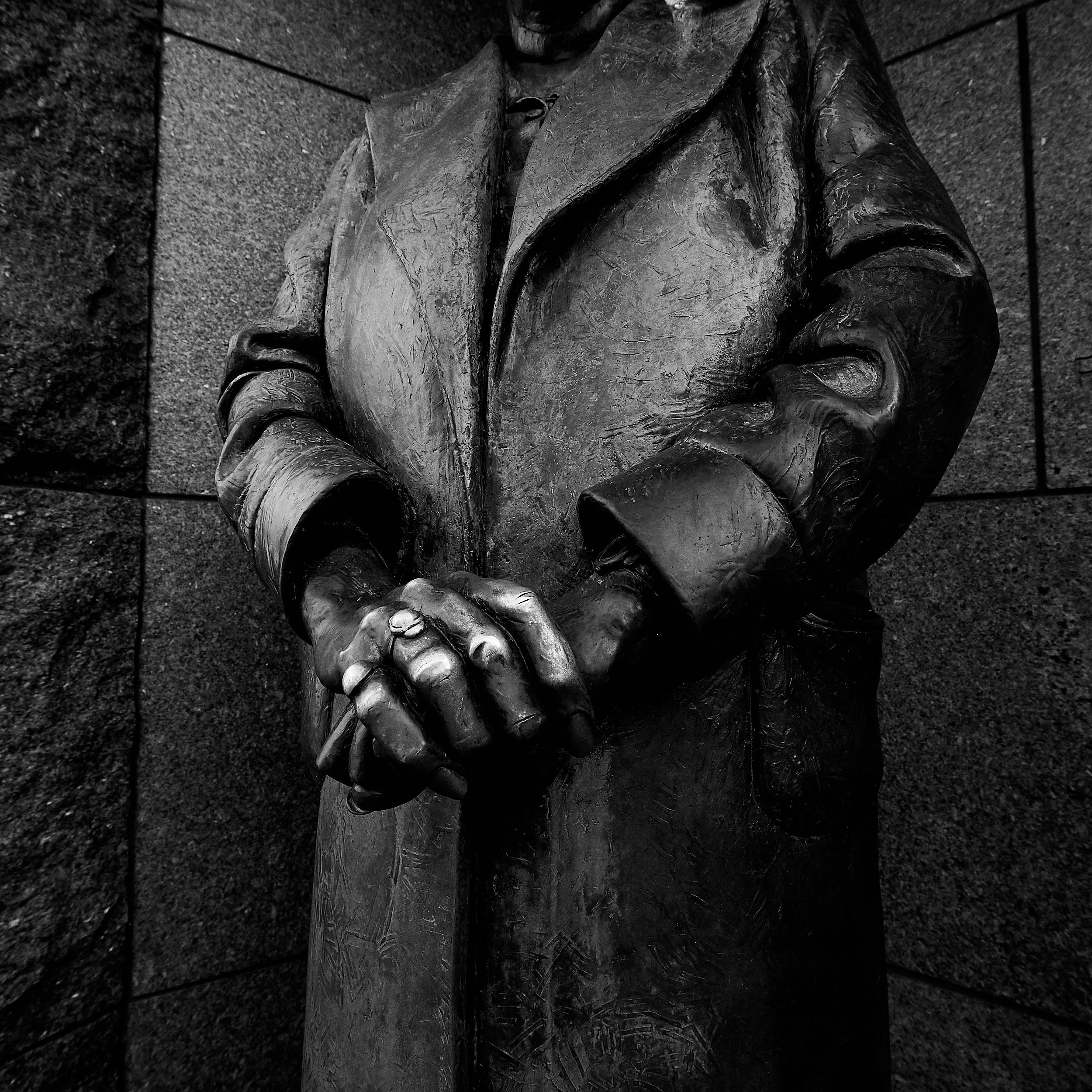 Close-up view of a bronze sculpture of two hands clasped together, mounted on a stone wall.