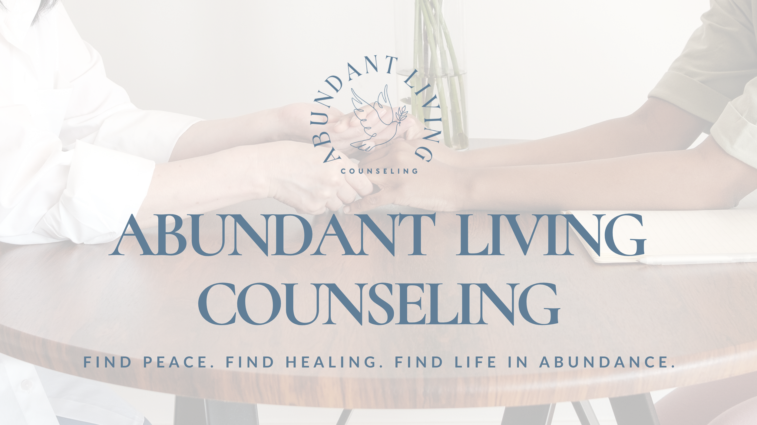 Two people sitting at a table, holding hands and engaging in a counseling session, with a logo of a dove and the words 'Abundant Living Counseling' overlayed on the image. The background is bright and clean, with a notebook and a vase with green stems on the table.