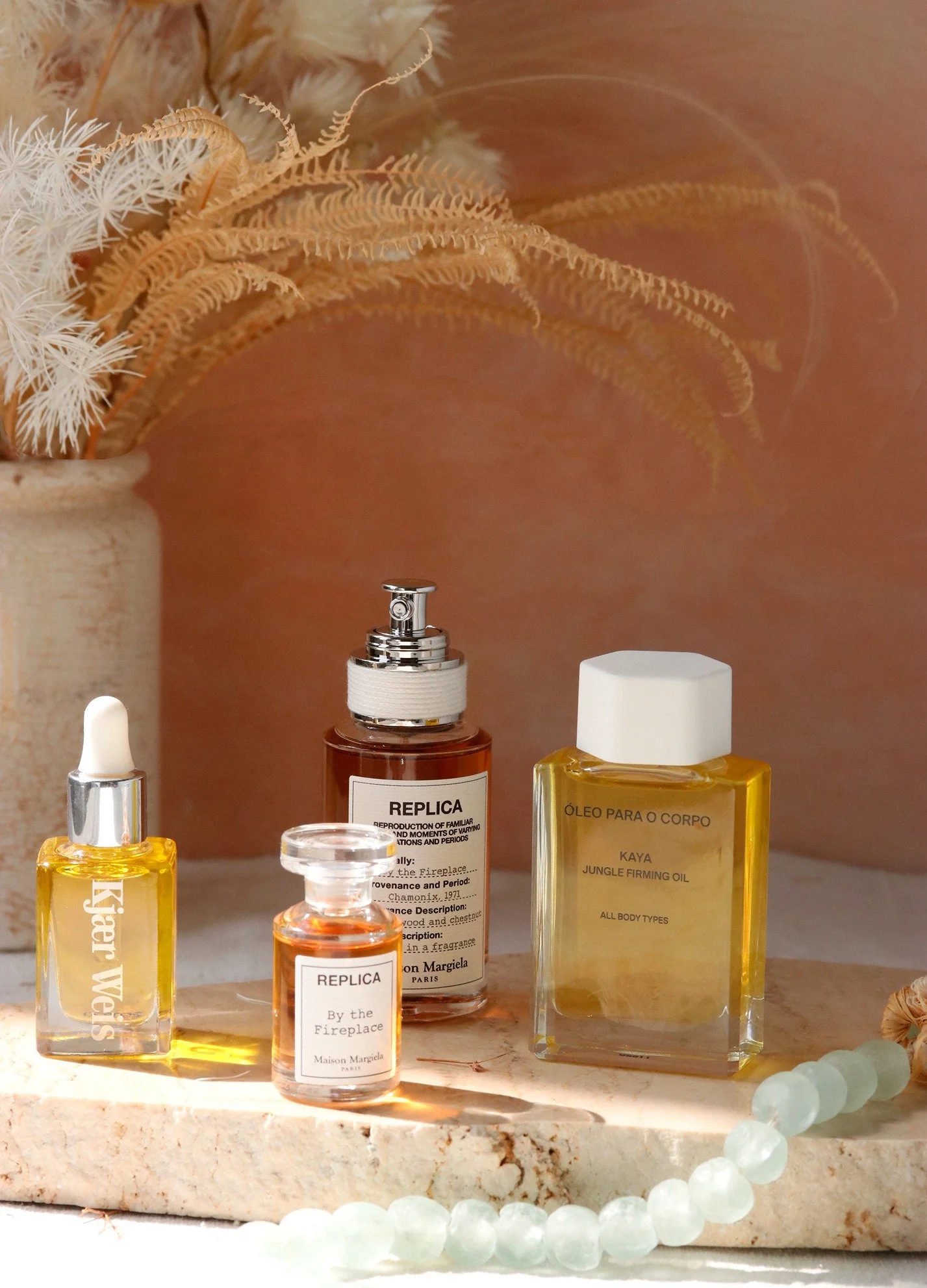 Various perfume bottles arranged on a marble surface with dried plants in a beige vase in the background.