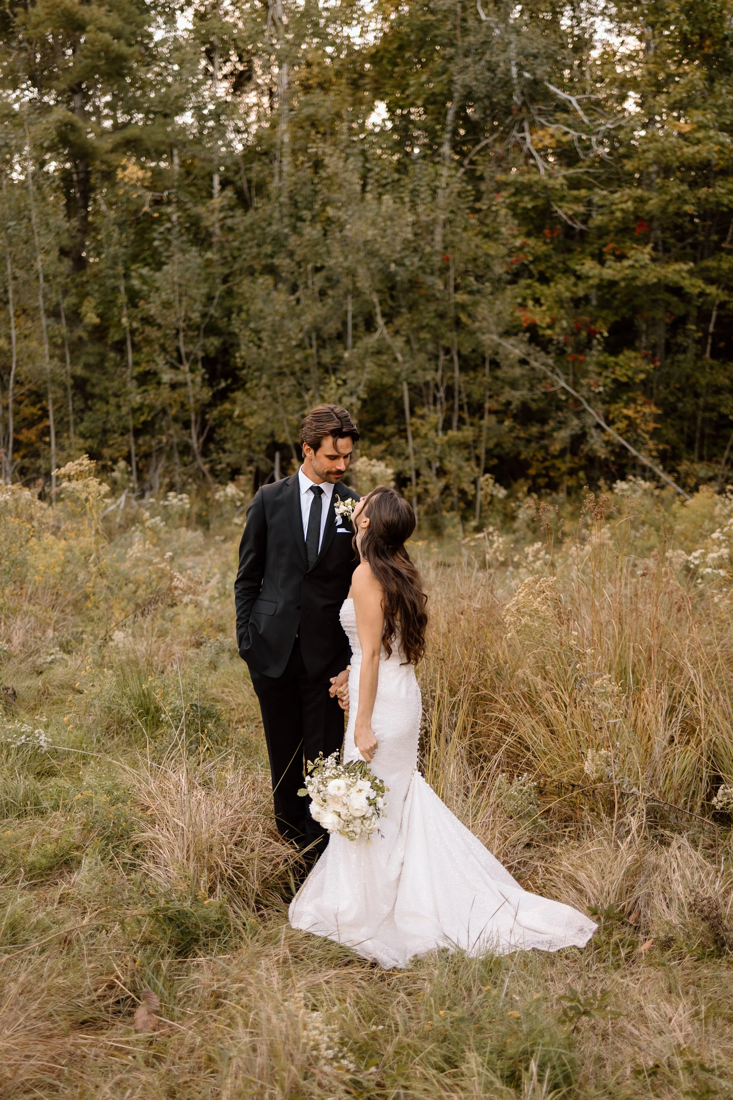 Newly wed couple, standing in tall grass gazing into eachother's eyes. Wedding photography of a newly married couple in Ontario Canada.