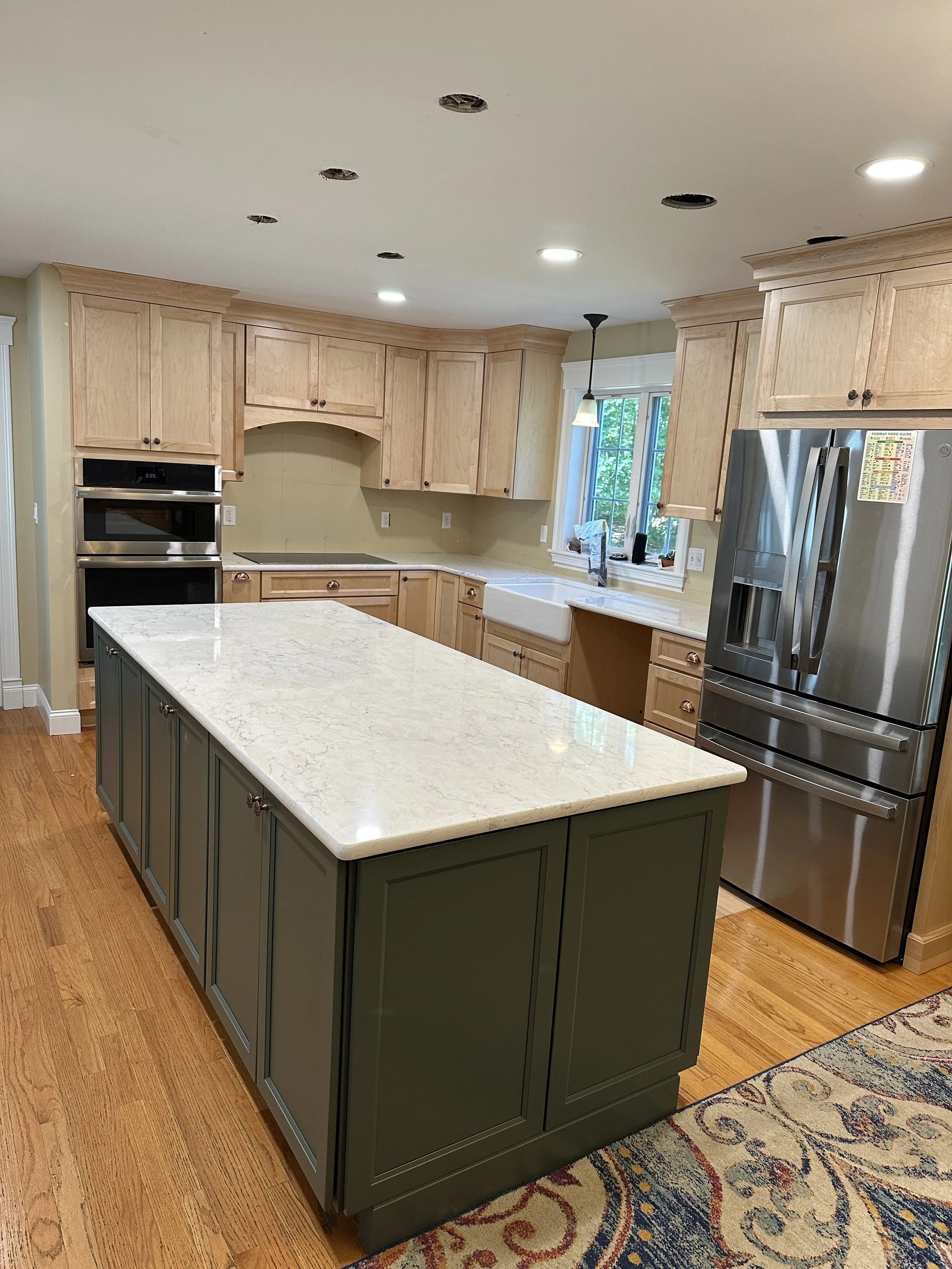 new kitchen upgrade renovation with wooden cabinets, a central island with a white marble top, stainless steel refrigerator, double oven, farmhouse sink, and hardwood floors. pendant lights, recessed lights